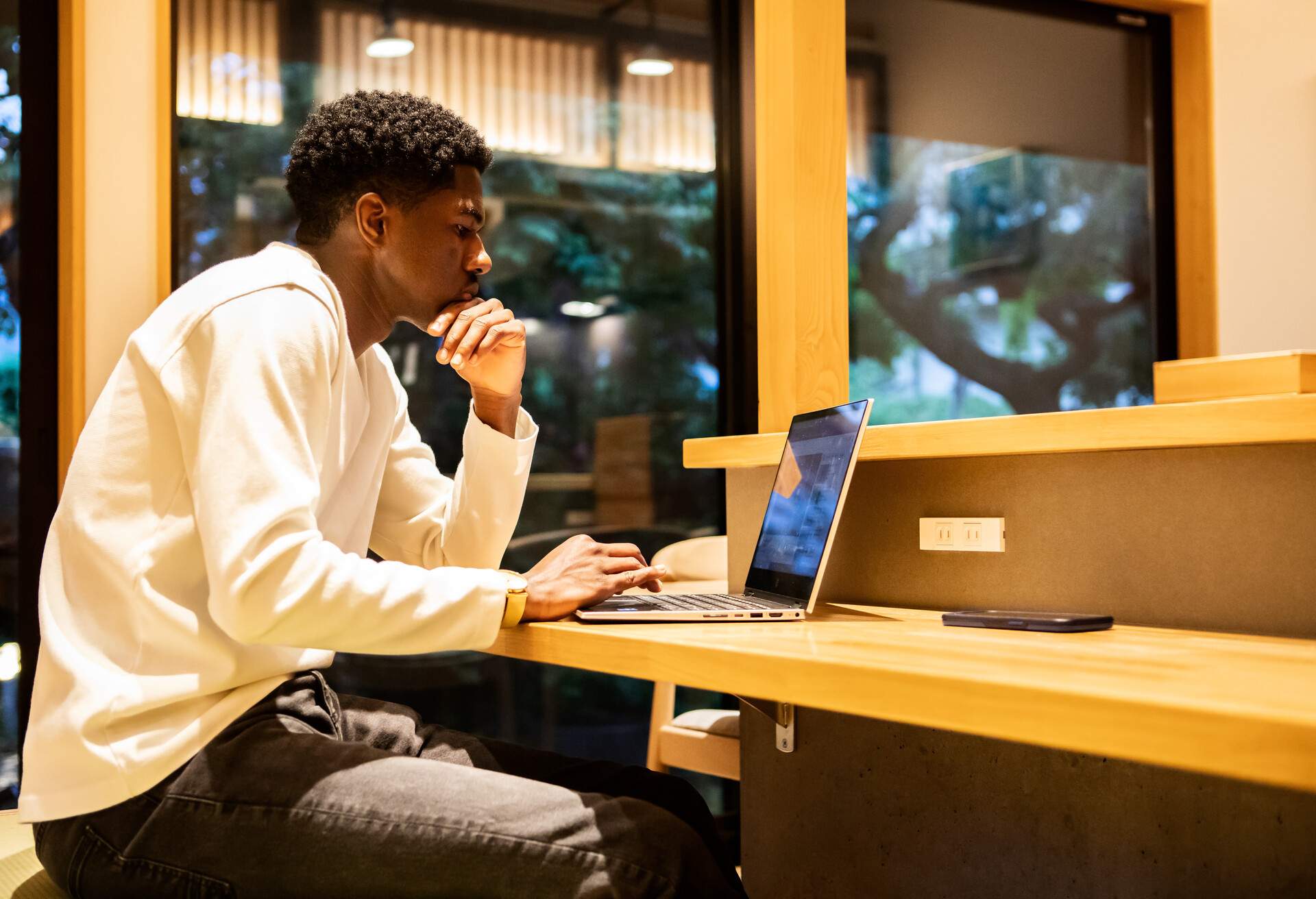 A young man sitting at a café, focused on his laptop.