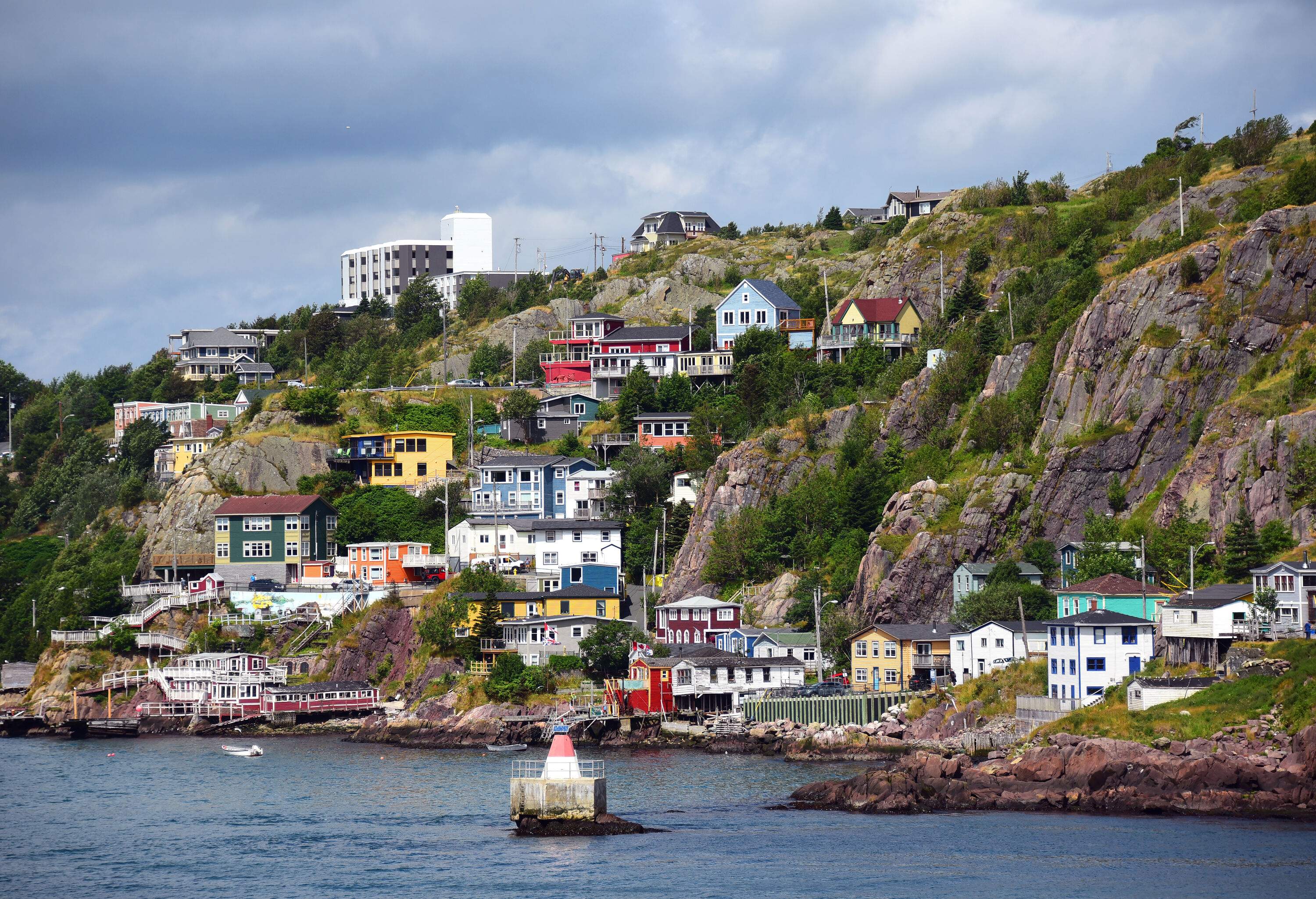Vibrant and colourful houses cascade on rugged slopes adorned with lush vegetation, nestled by the picturesque coast.