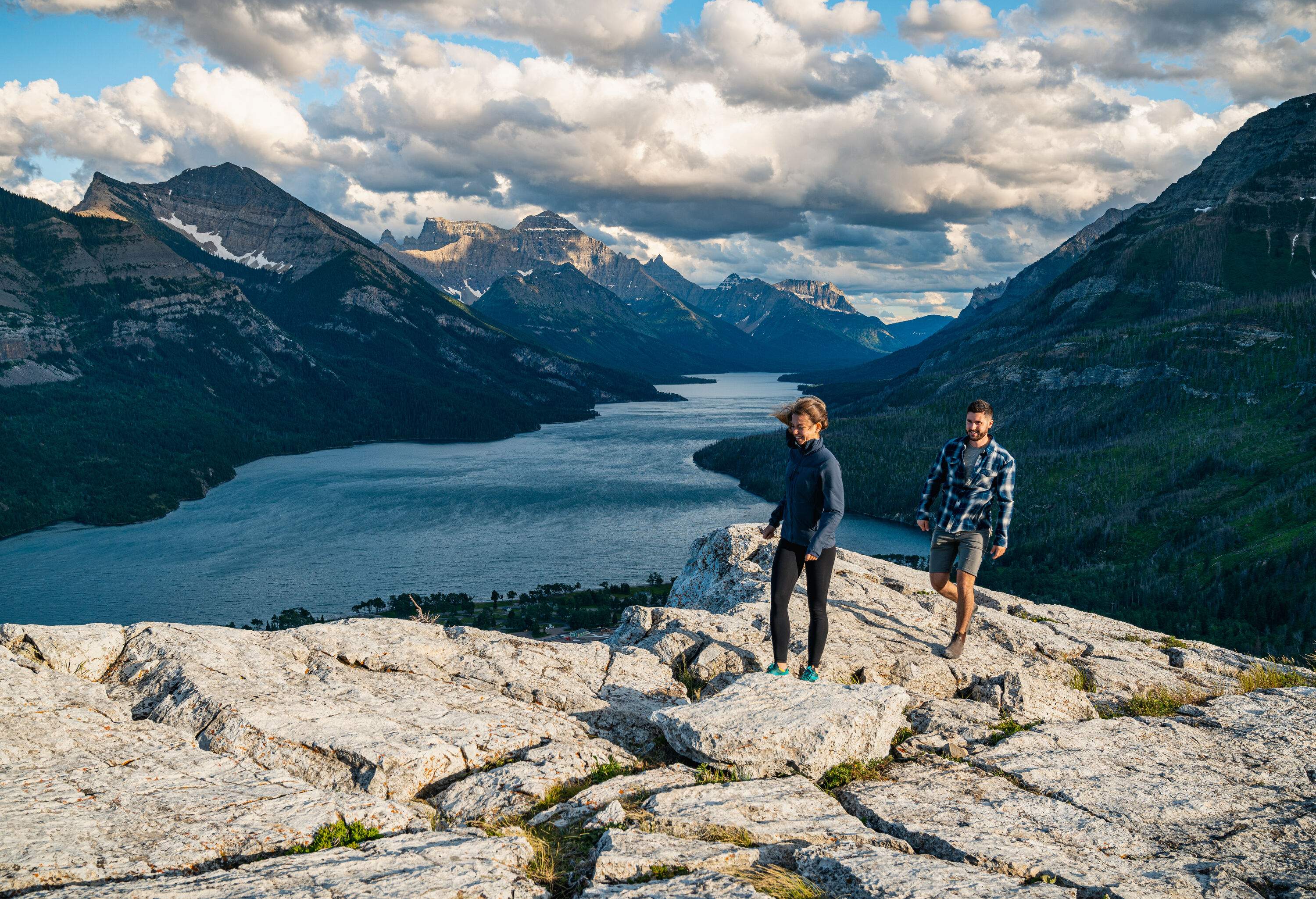 A couple hiking on a rocky summit with overlooking views of a lake between the valleys.