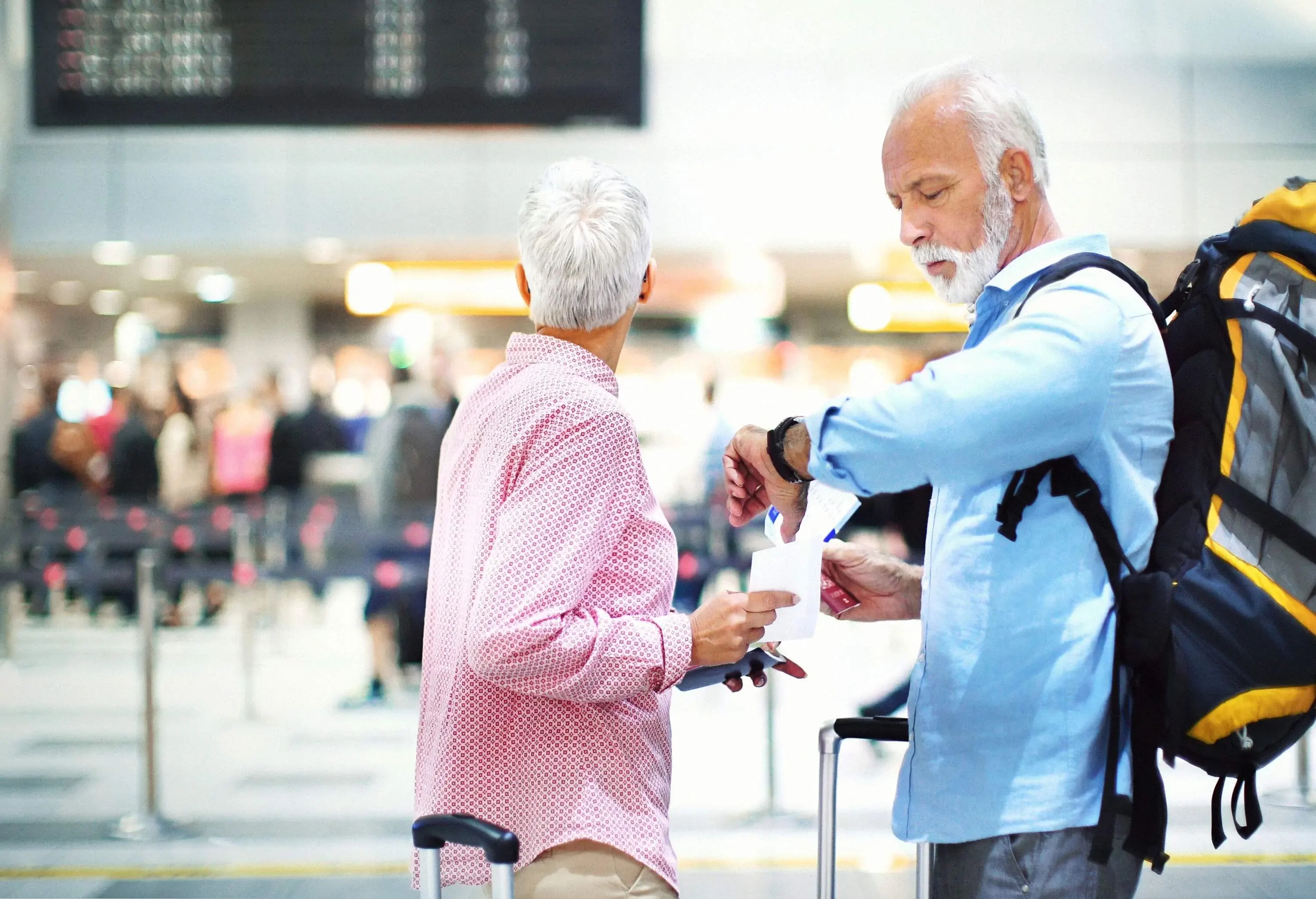 An older couple arriving at the airport and checking the departures board.