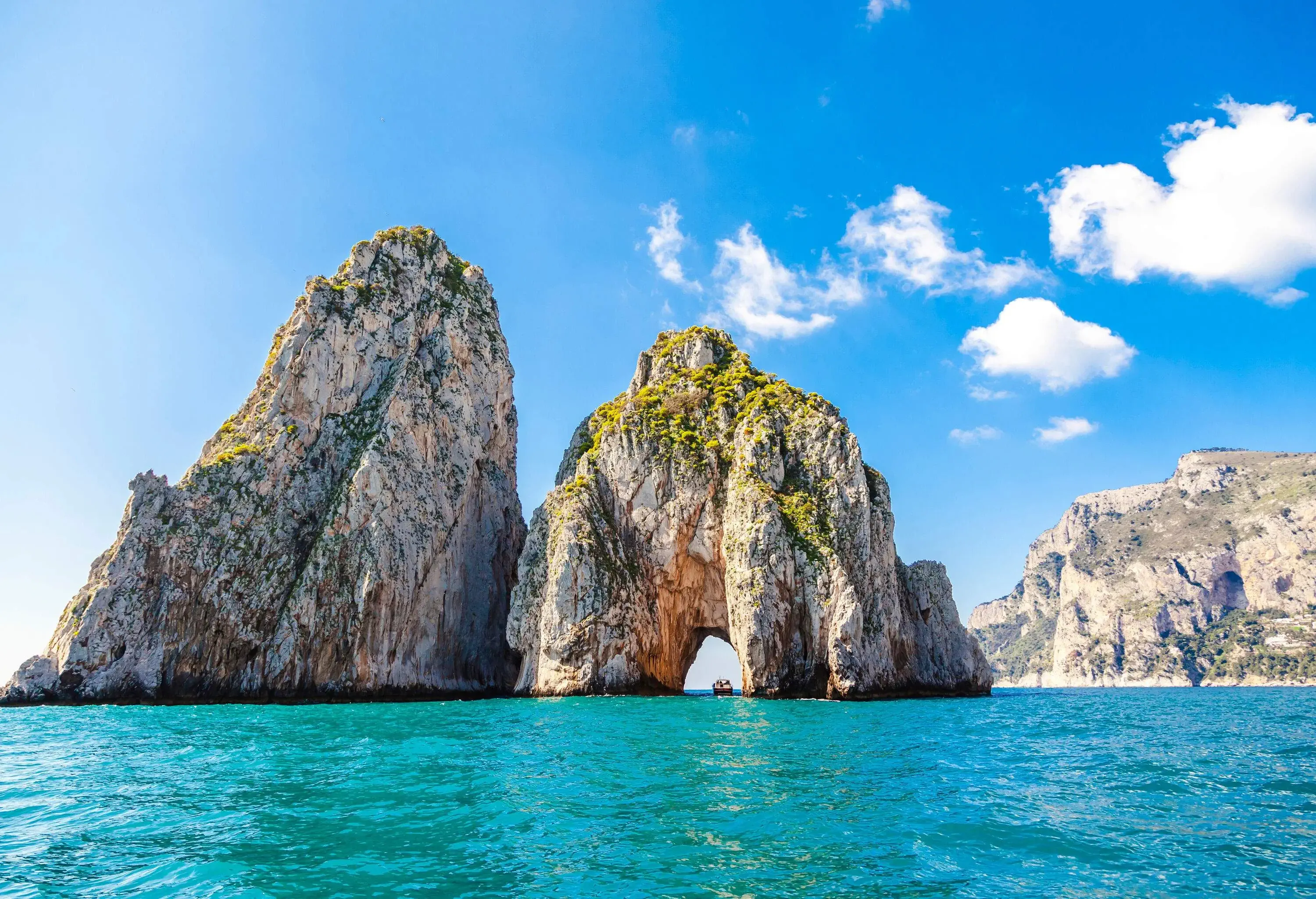 Two massive rock formations in the ocean, one with an arch opening.