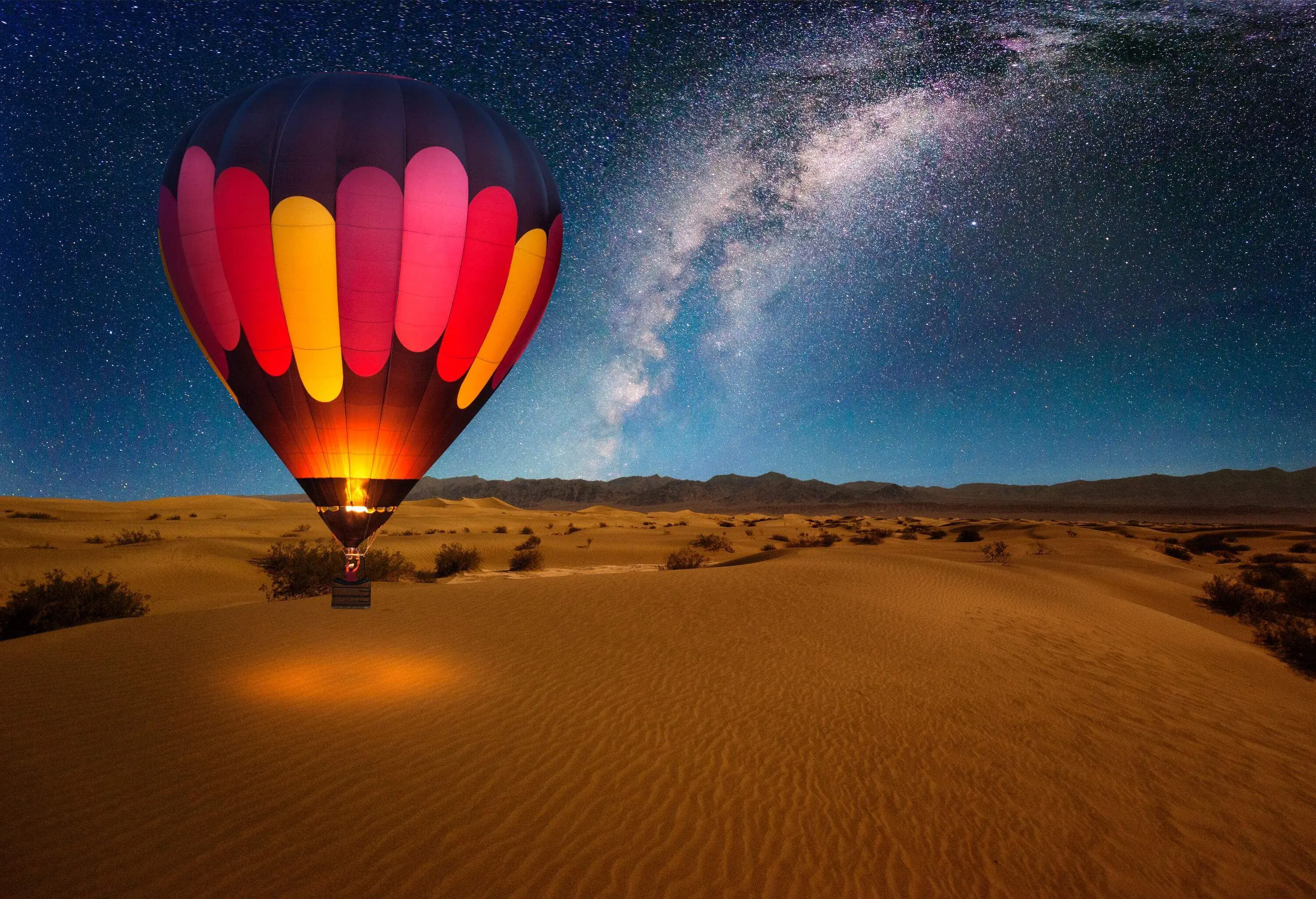 A majestic hot air balloon soaring gracefully under the starry Milky Way, floating serenely over a vast desert landscape, creating a breathtaking nighttime scene.
