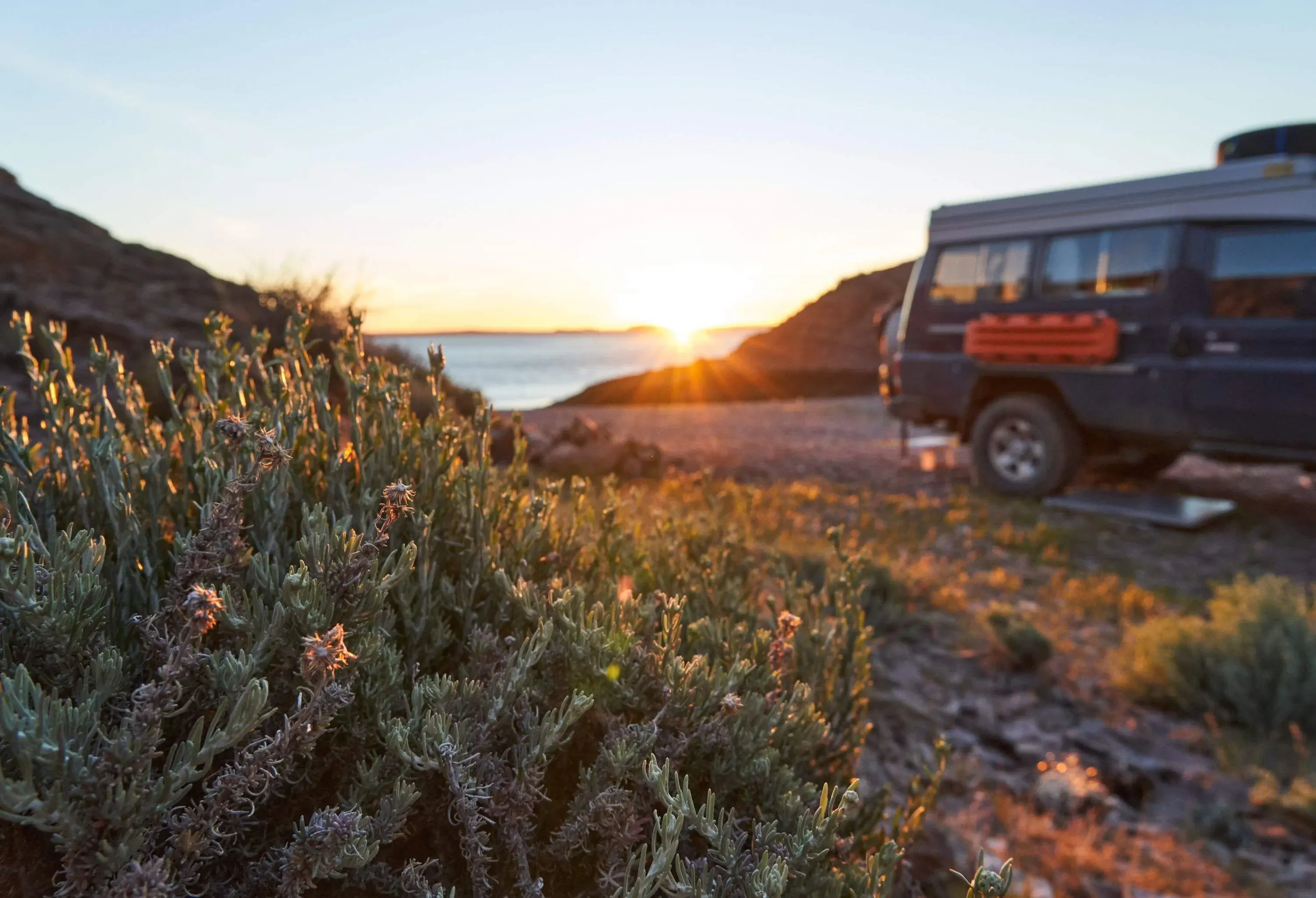 Focus an a dry shrub with a blurry blue truck in the backgound with golden sunset over the Deseado river at Puerto Deseado in Patagonia Argentina