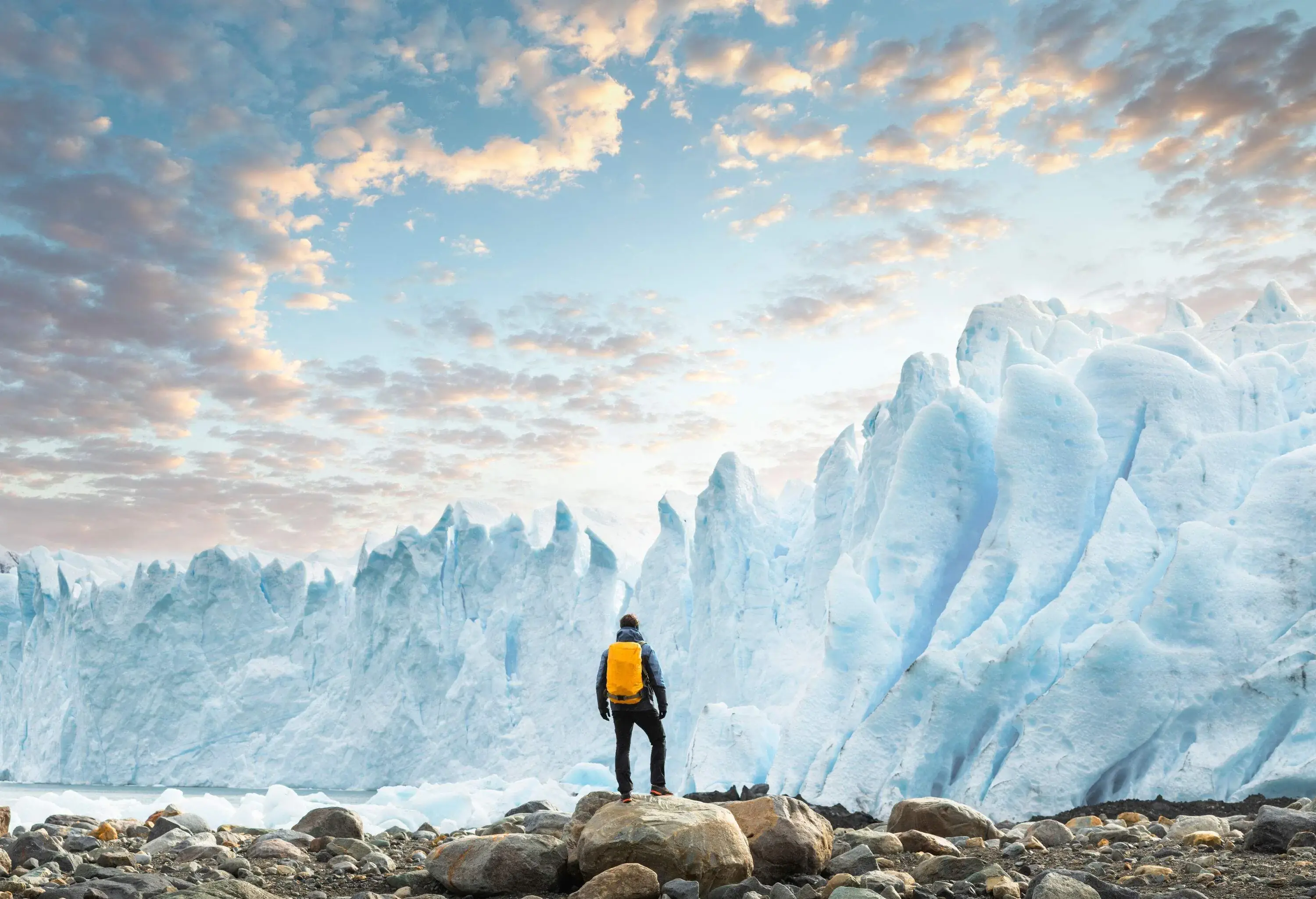 A hiker with a yellow backpack standing on a rock and looking at a wall ice formations.