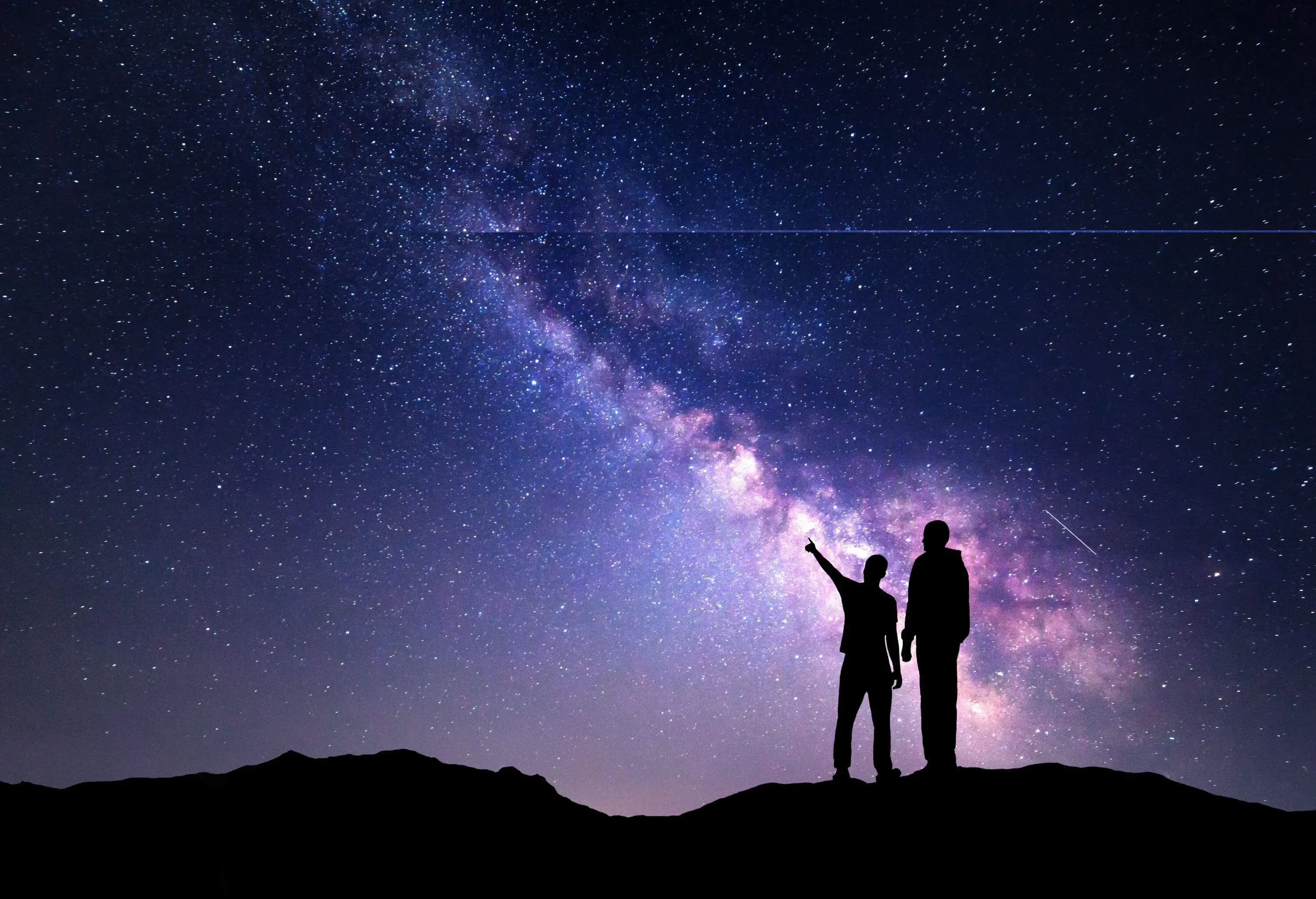Milky Way with silhouette of a family on the mountain. Father and a son who pointing finger in night starry sky. Night landscape. Beautiful Universe. Space. Travel background with sky full of stars