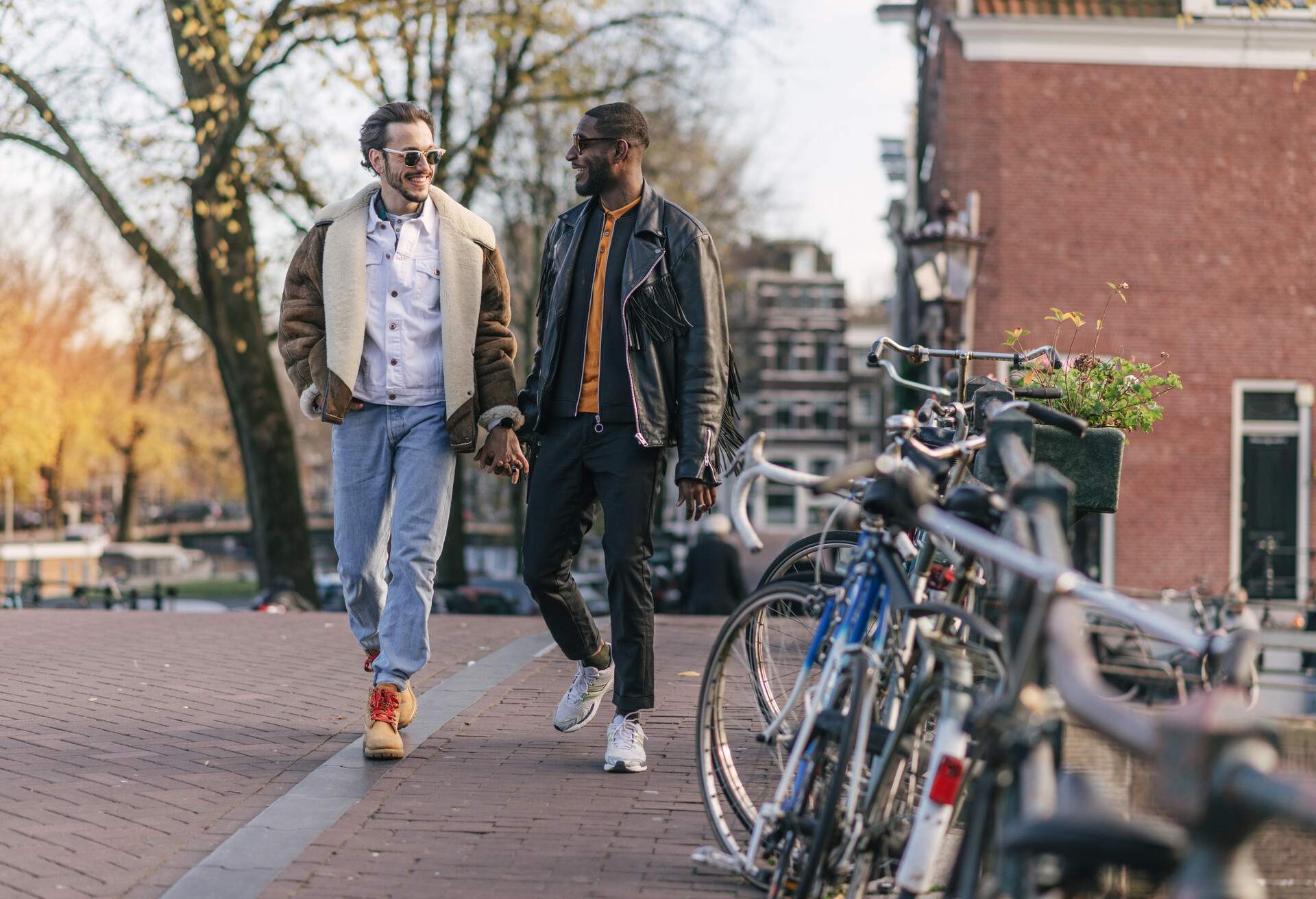 A gay couple in winter clothes walk hand in hand down a cobbled street lined with parked bicycles, Amsterdam, The Netherlands