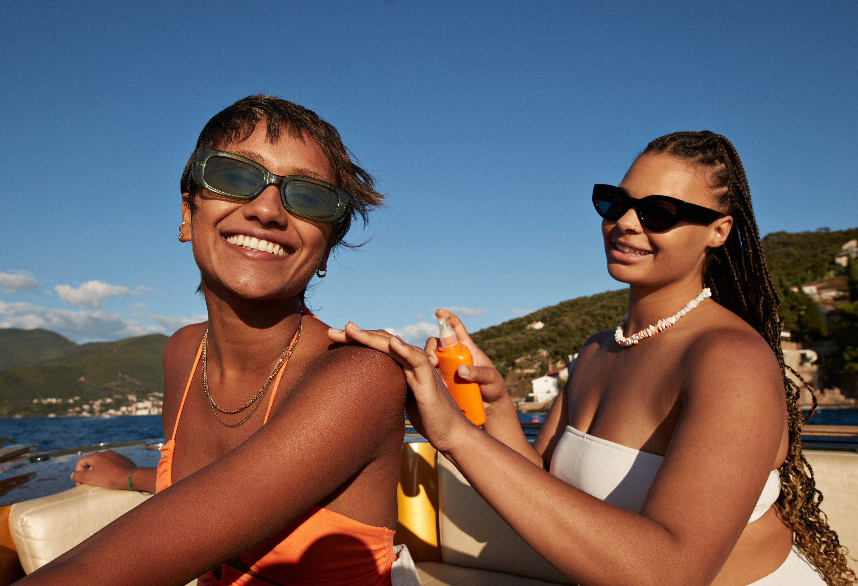 Young woman applying sunscreen on female friend's shoulder sitting in motorboat during sunny day