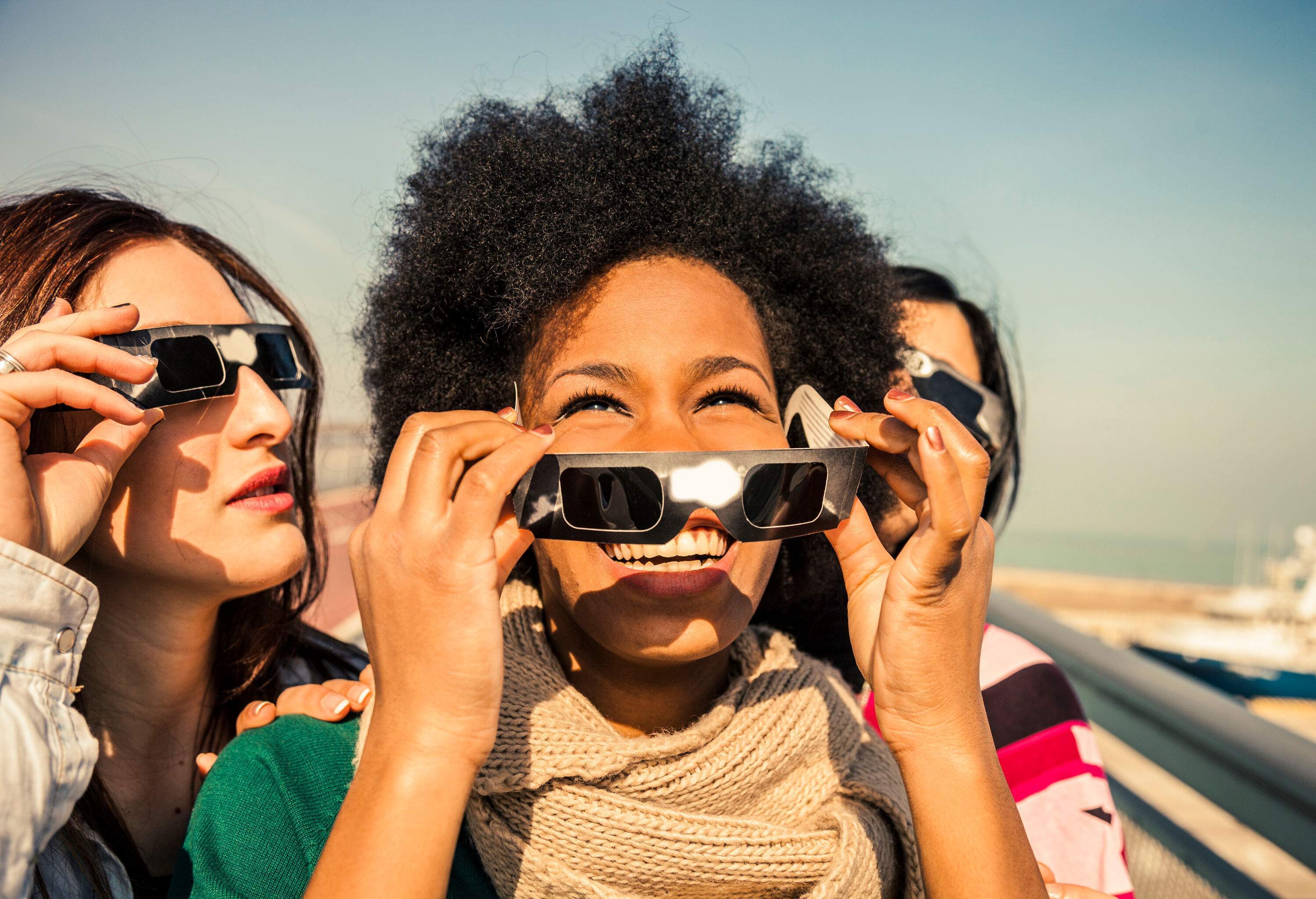 Group of female friends have fun together during a solar eclipse event. Their looking and pointing to the sun wearing the typical glasses normally used to watch a solar eclipse.