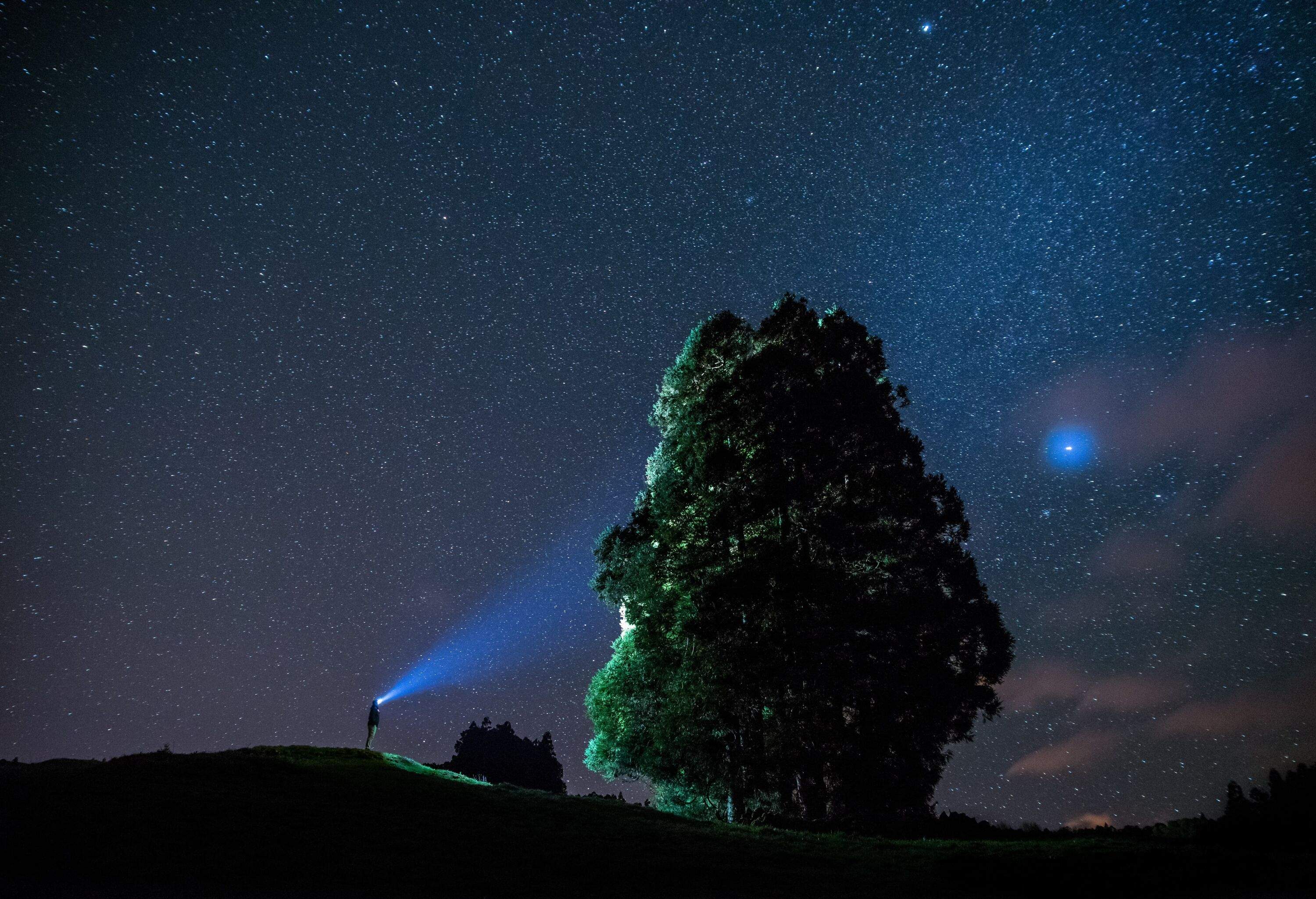 Night sky over the Azores, man with flashlight lighting up a giant rock