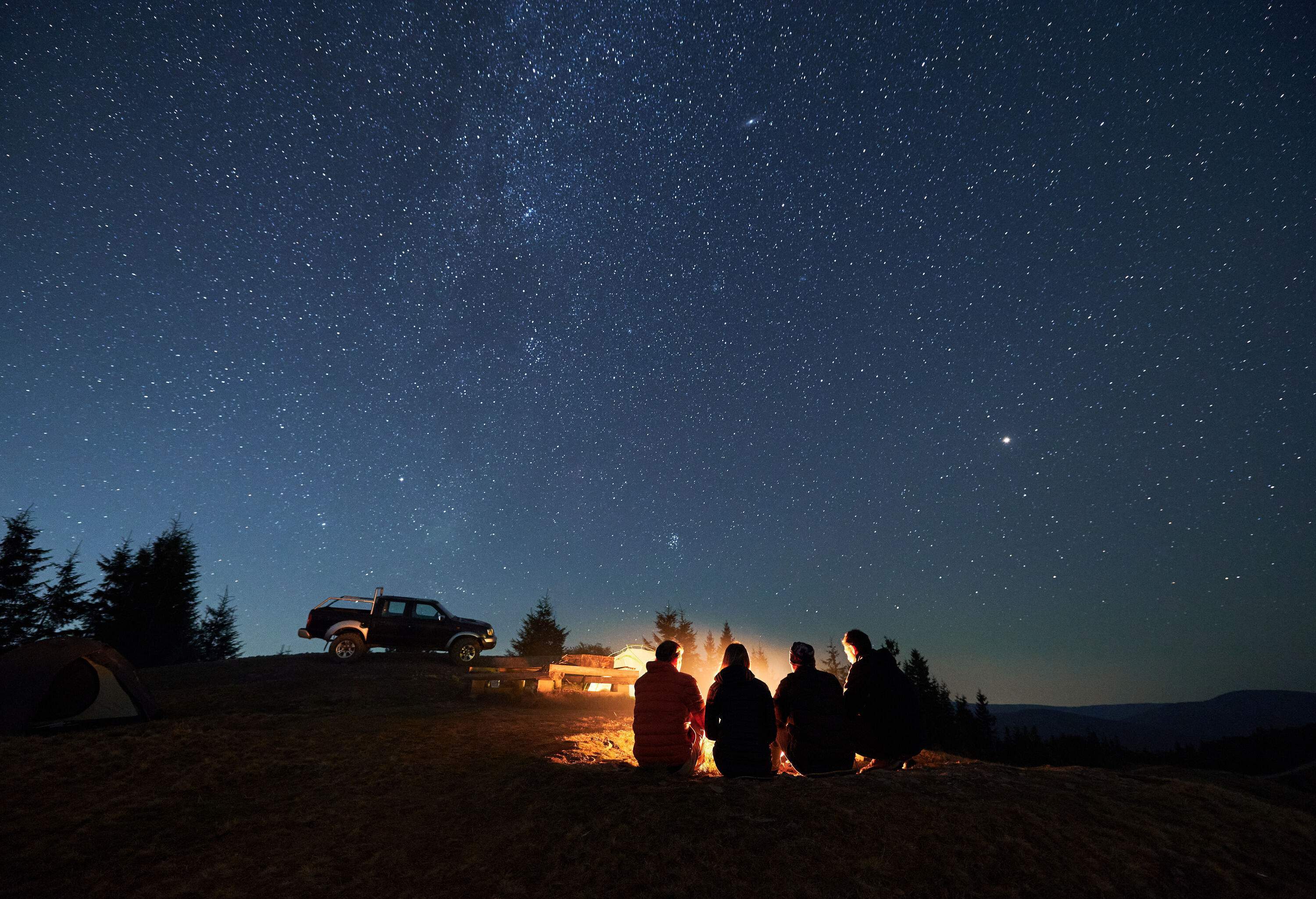 Four people gathering around a campfire under a star-studded night sky.