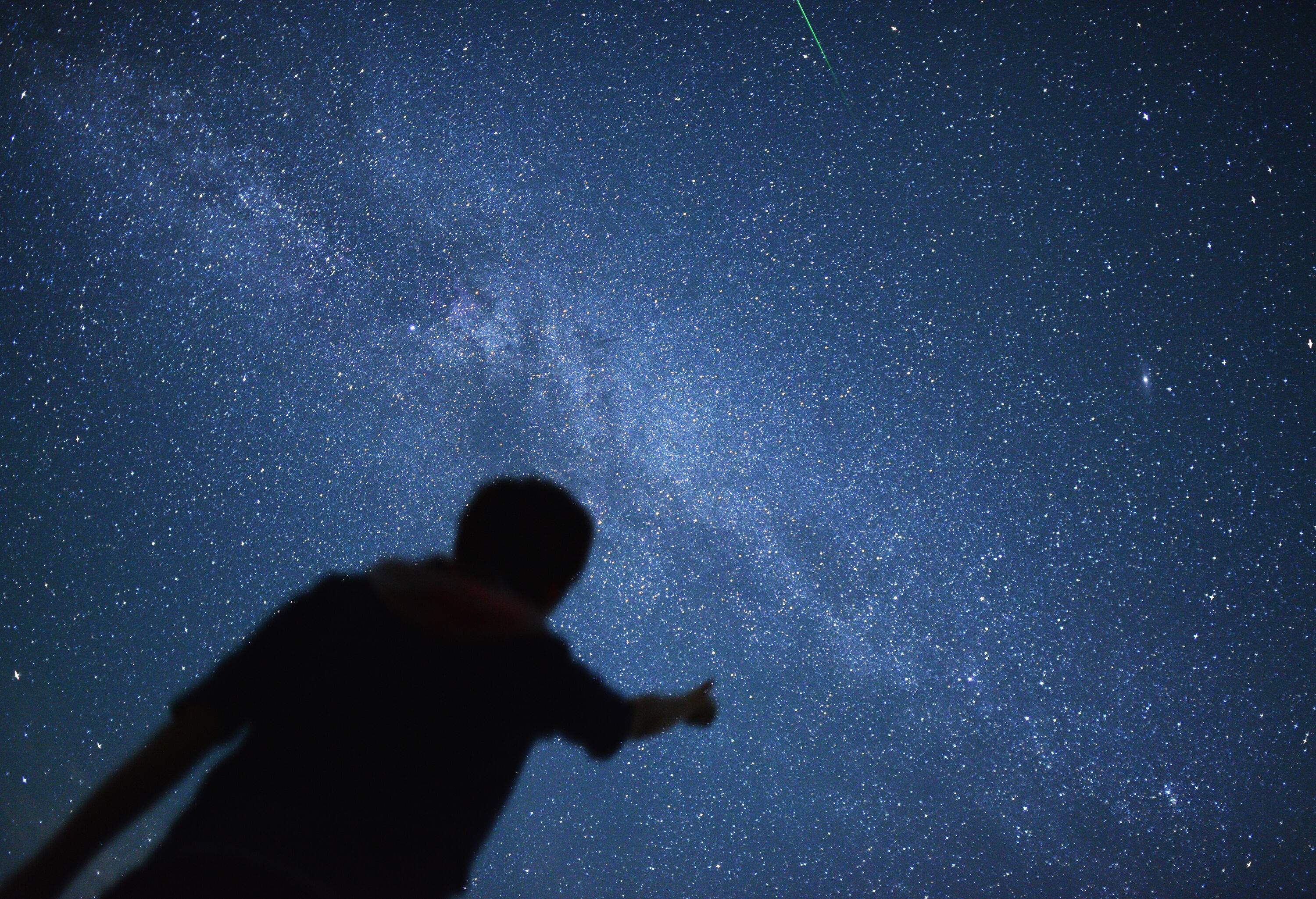 Silhouette of a person pointing at a constellation of stars.