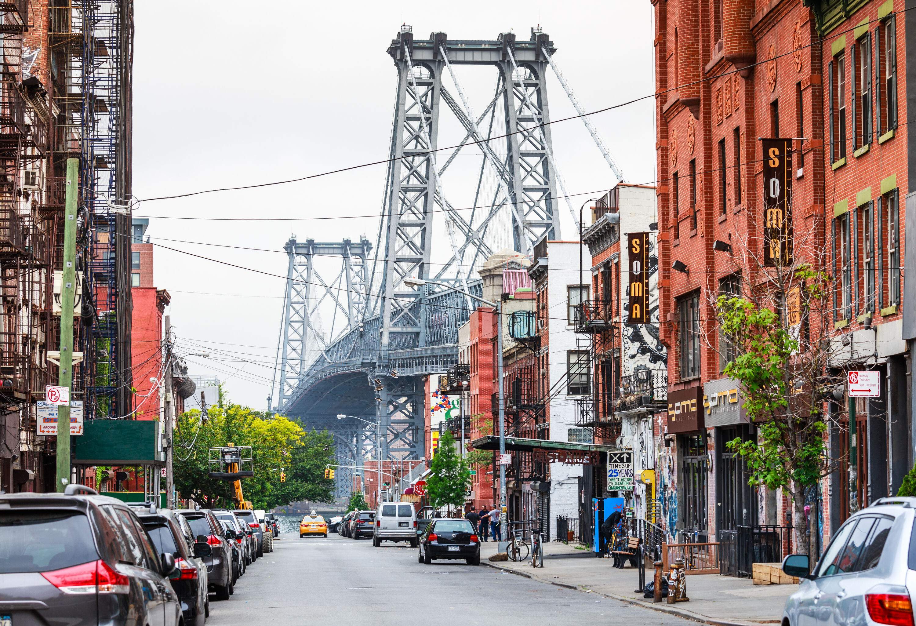 The two tall steel towers of a suspension bridge visibly seen lined up with a row of commercial buildings alongside the street.