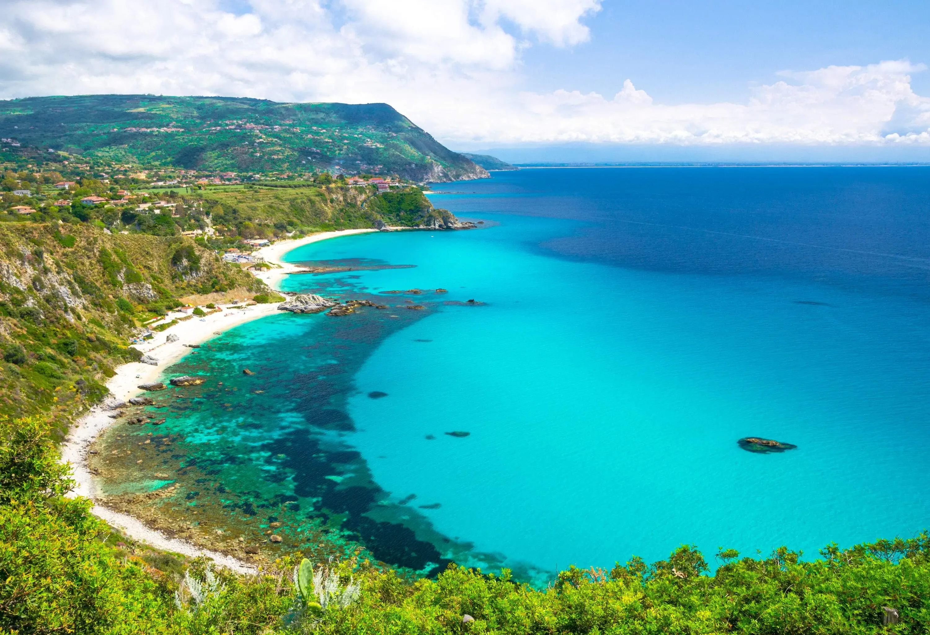 A breathtaking ocean view with crystal clear blue water bounded by lush green steep mountains.