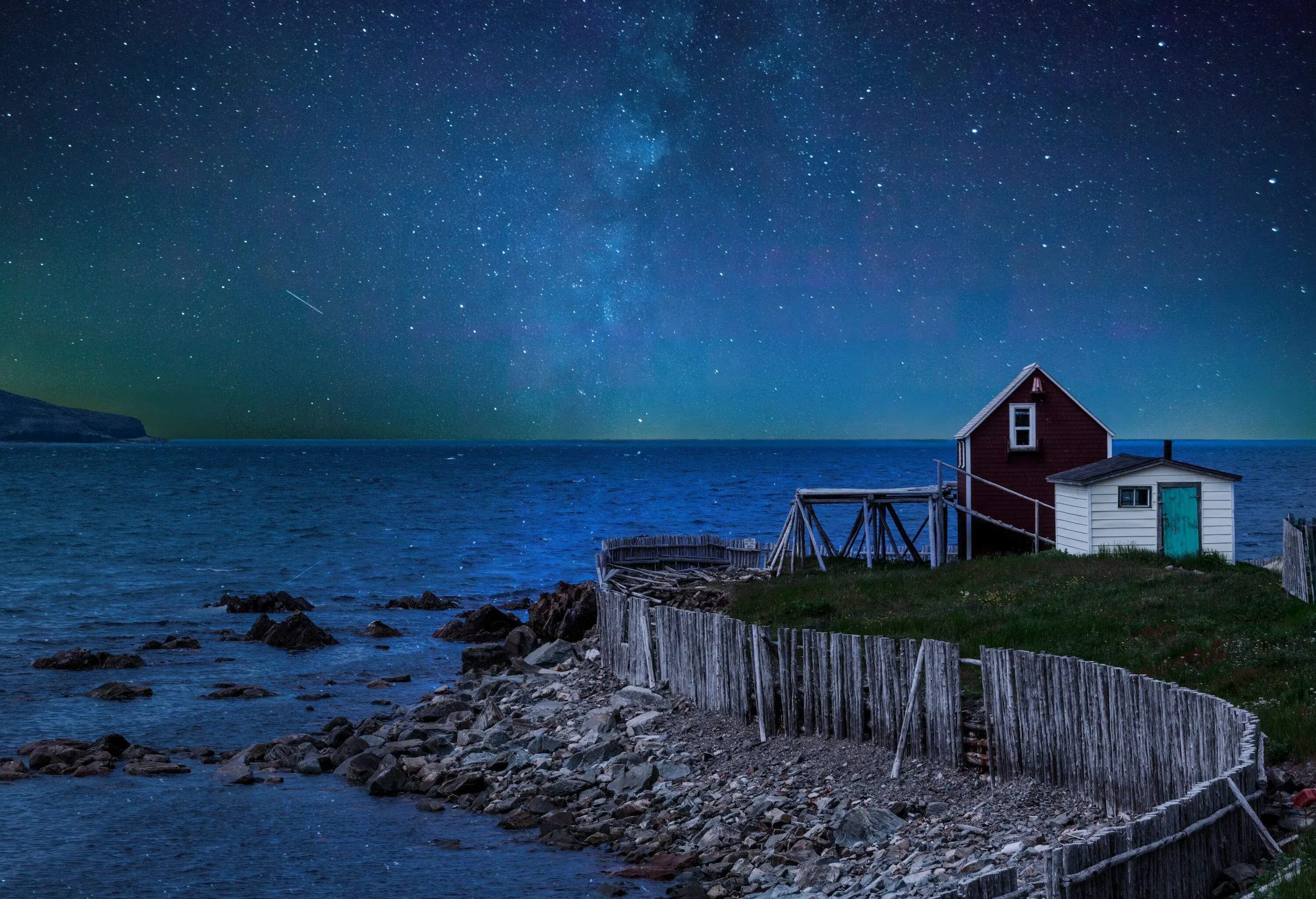 Small fishing hut over a dock by the beach at night under a starry sky