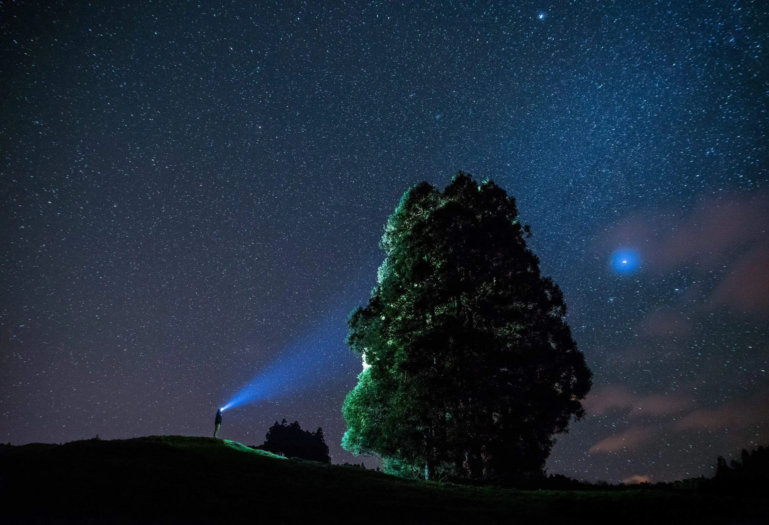 Night sky over the Azores, man with flashlight lighting up a giant rock