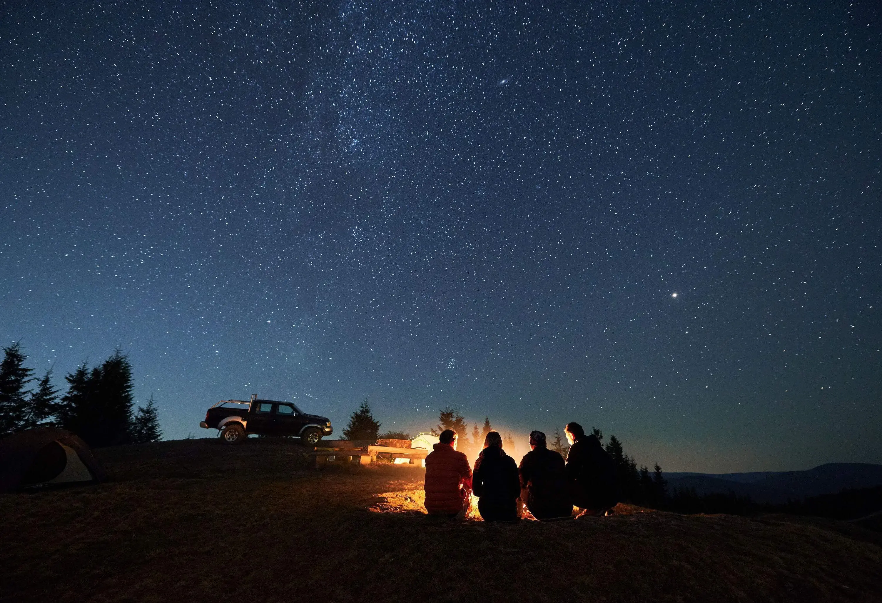 Four people gathering around a campfire under a star-studded night sky.
