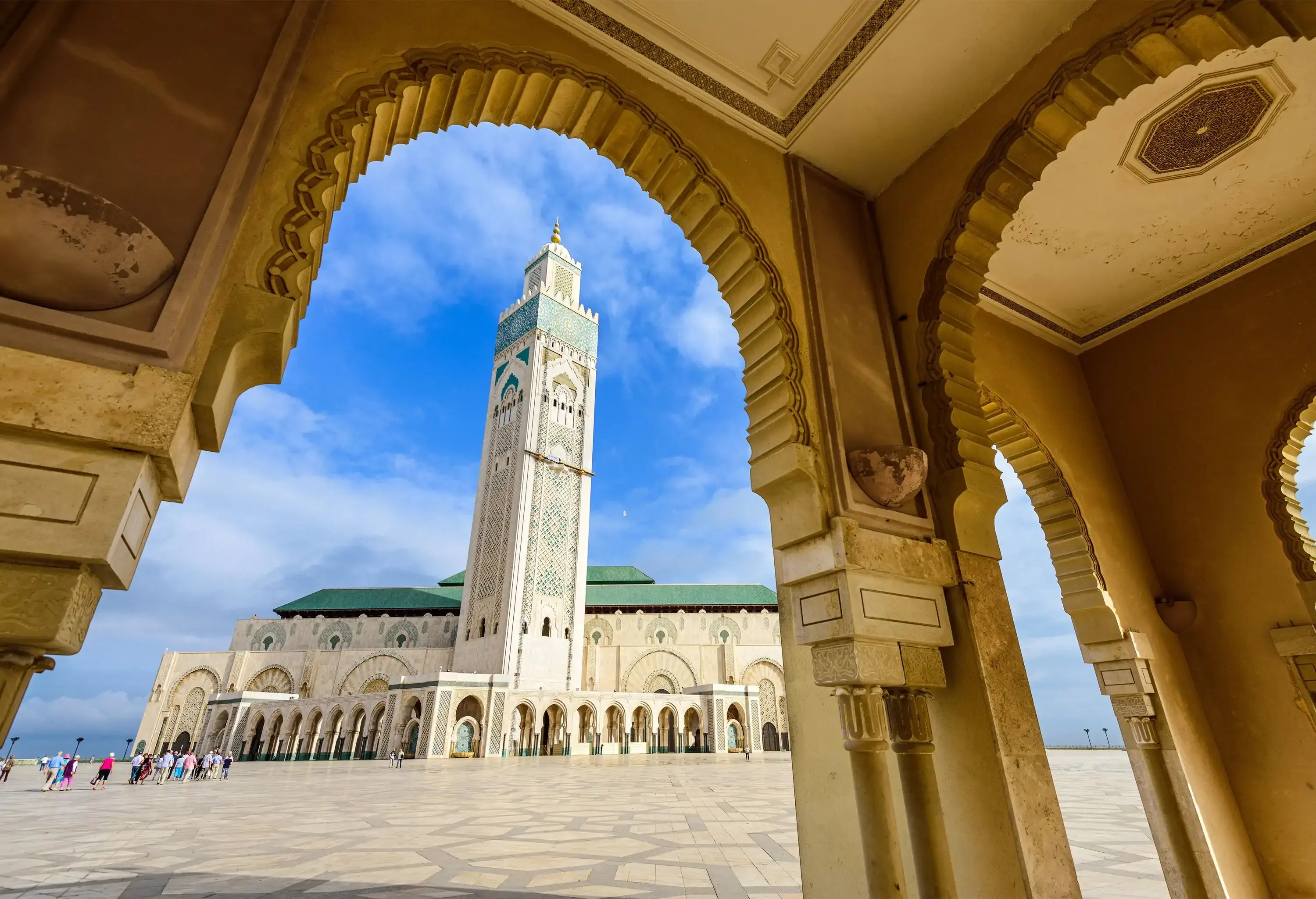 An elaborate mosque with intricate decor and a towering minaret in the centre against the cloudy blue sky.