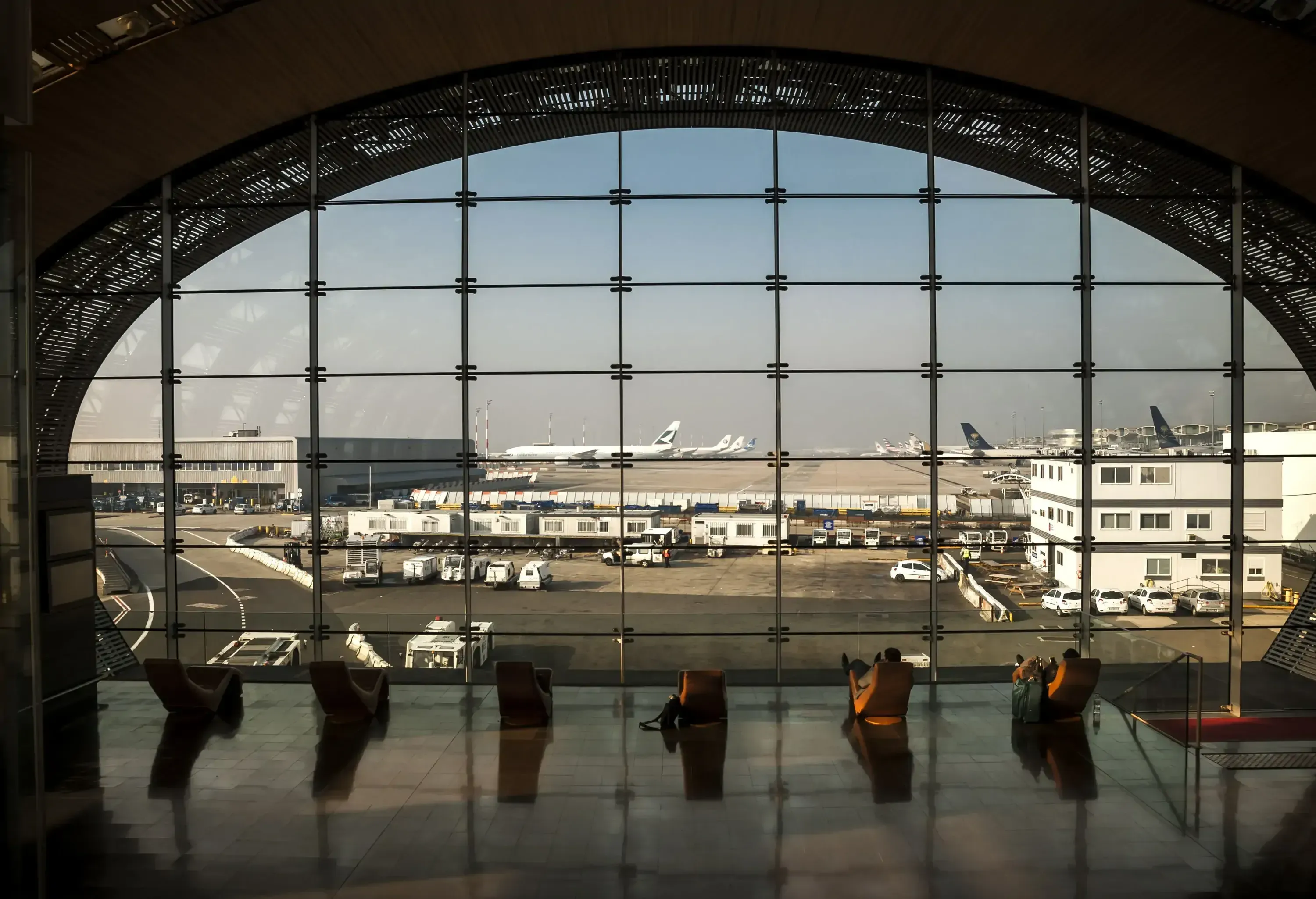 People sitting in loungers at an airport terminal overlooking the tarmac.