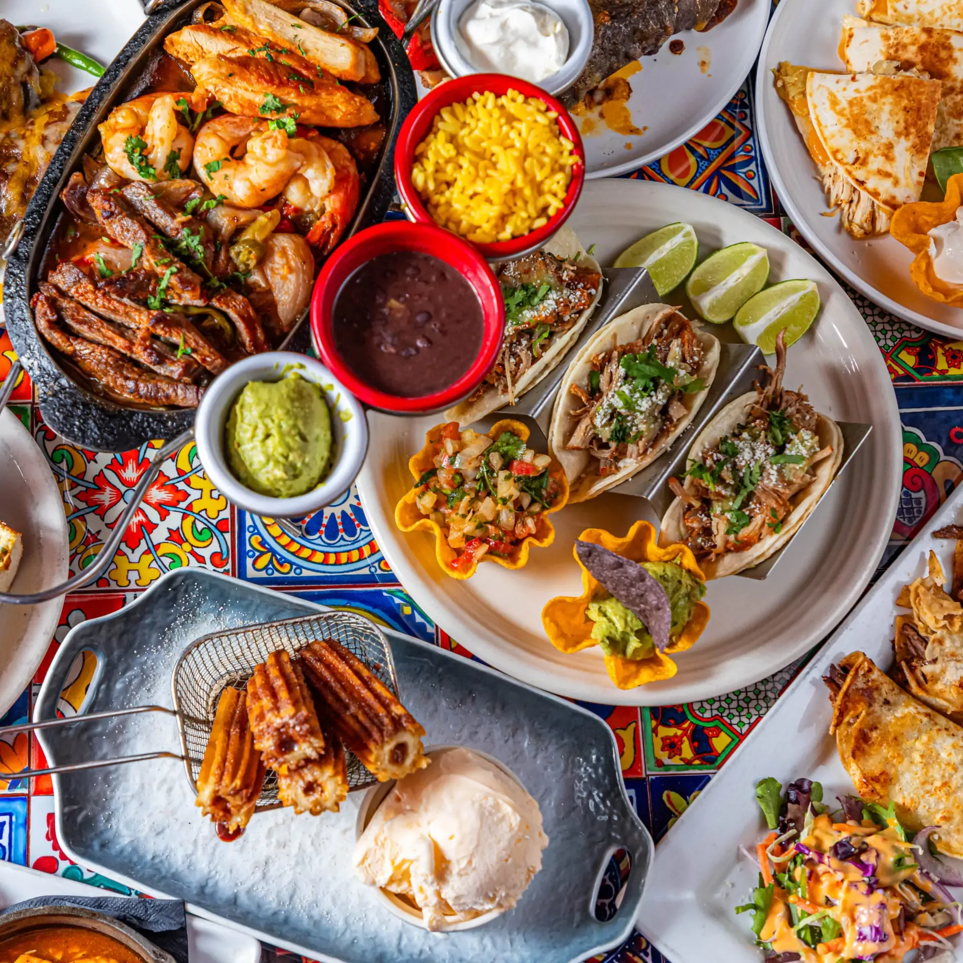 A delicious spread of Mexican food including tacos, fajitas, churros, and sides on a colorful table.