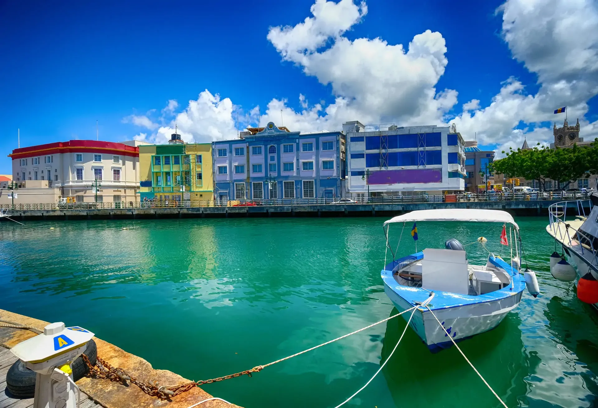 Colorful buildings line a harbor with a white boat floating on clear turquoise water.