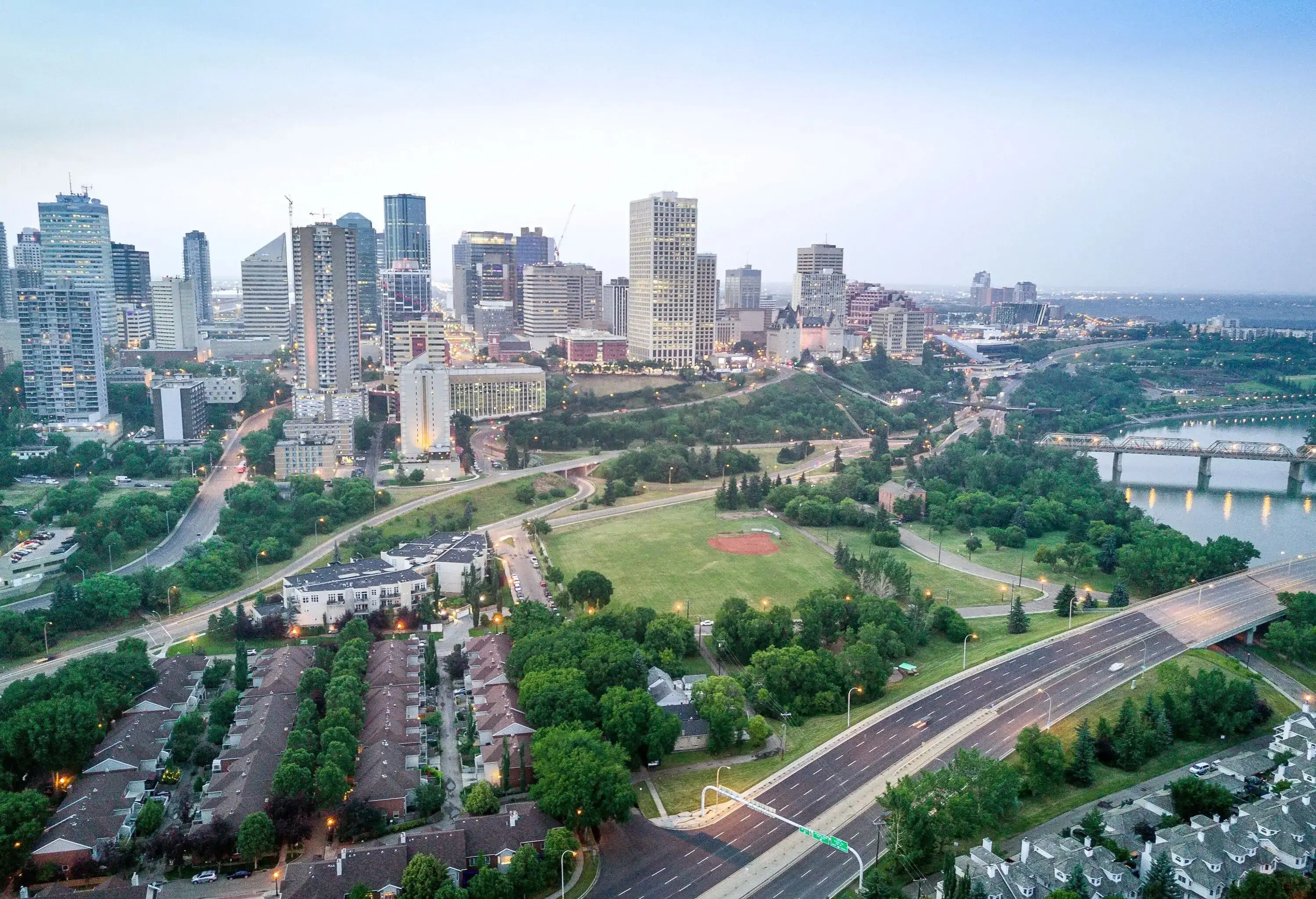 Tall compact buildings cluster along a lush park alongside a river spanned by several bridges.