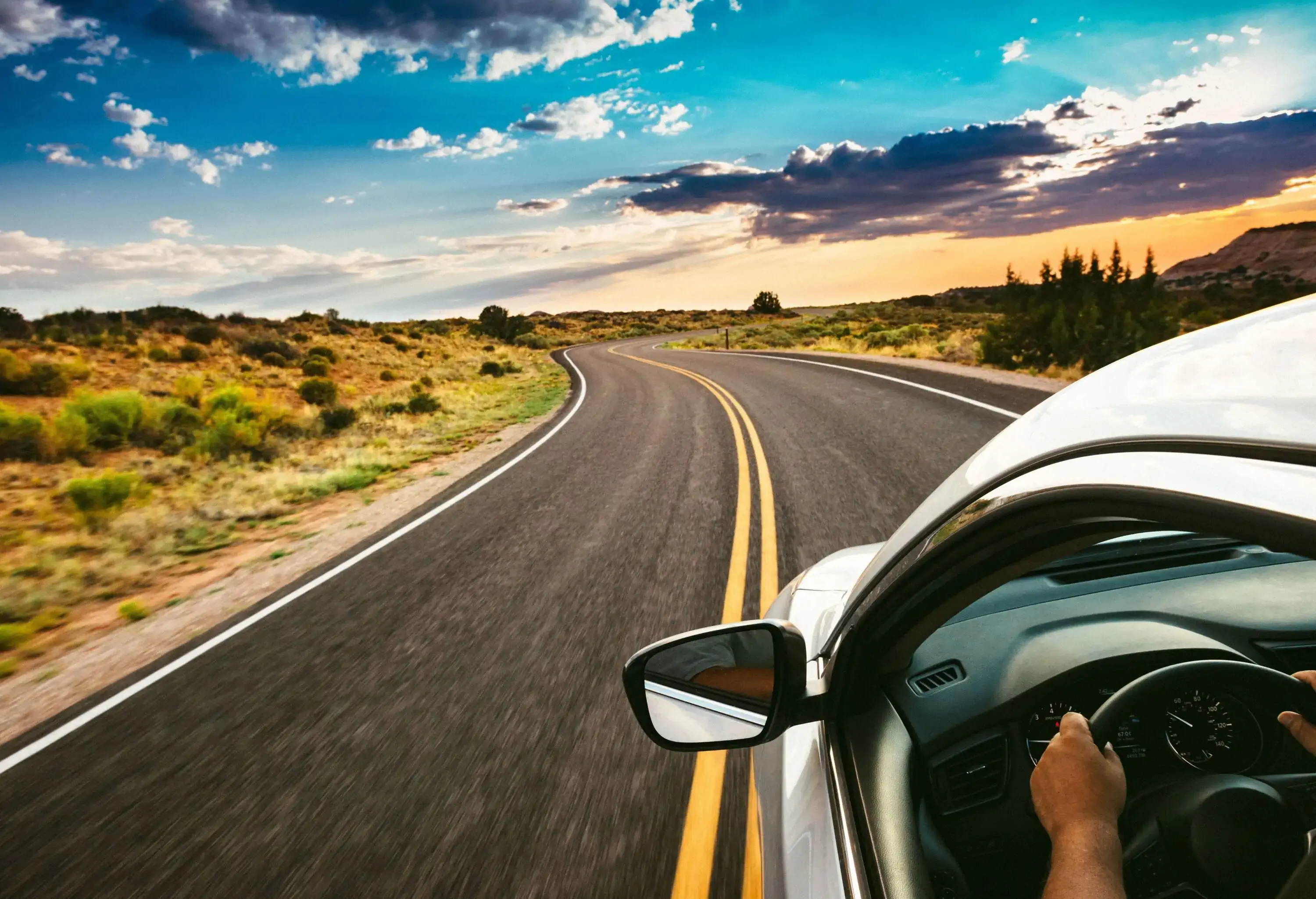 A man driving his car down an empty road under a beautiful sky.