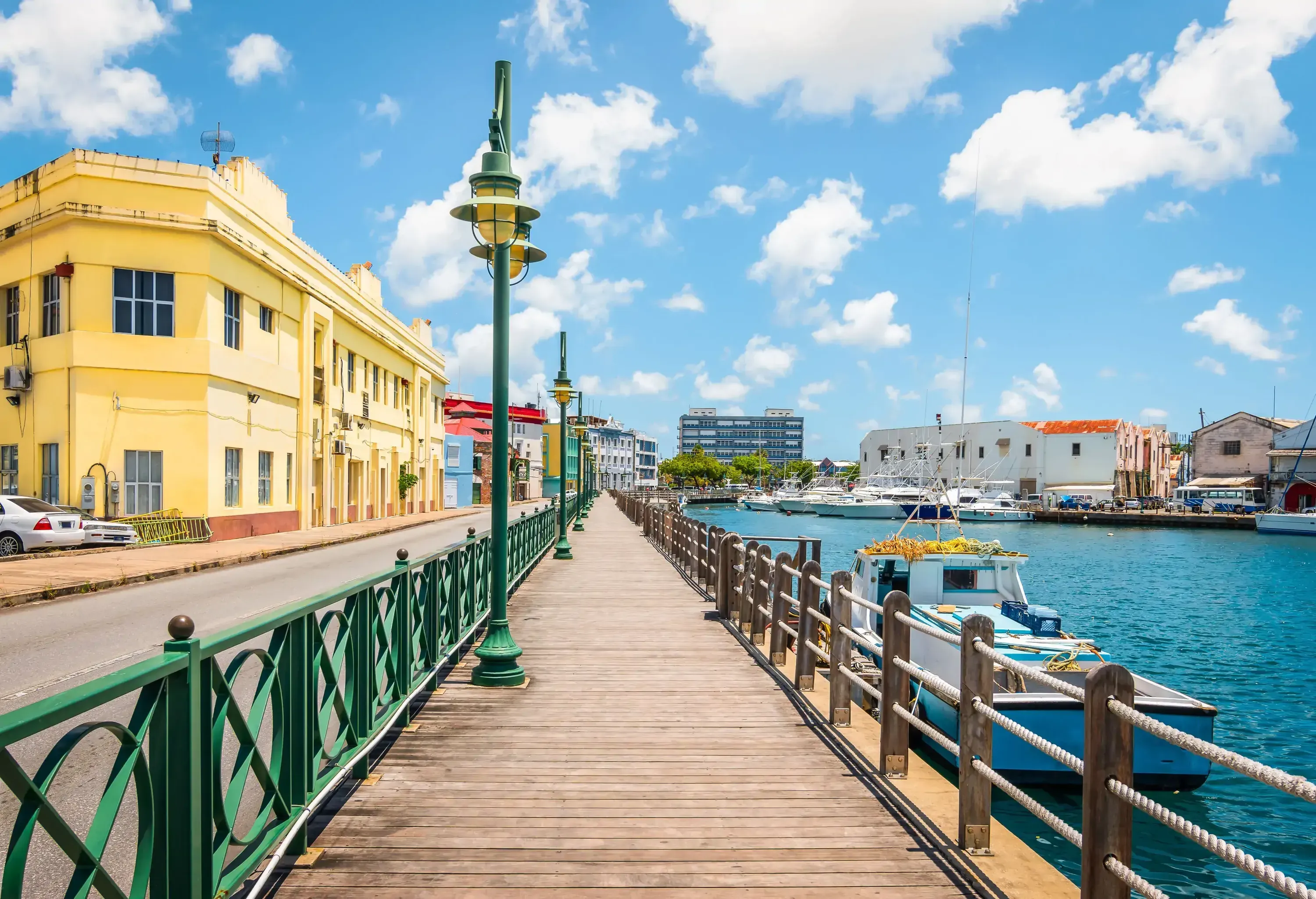 A boardwalk with green street lamps running on the a harbour.