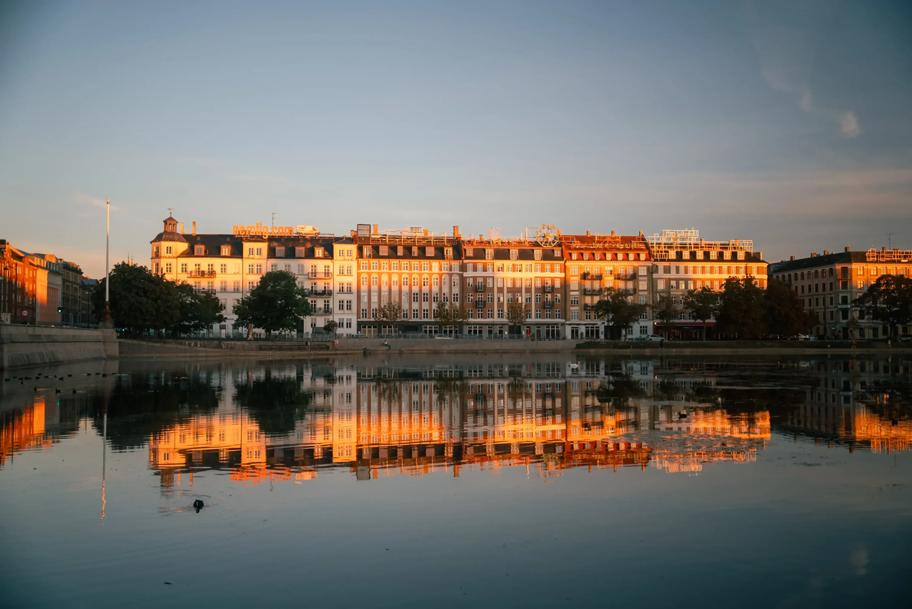 Golden sunset light reflecting European city buildings onto a calm river at dusk.