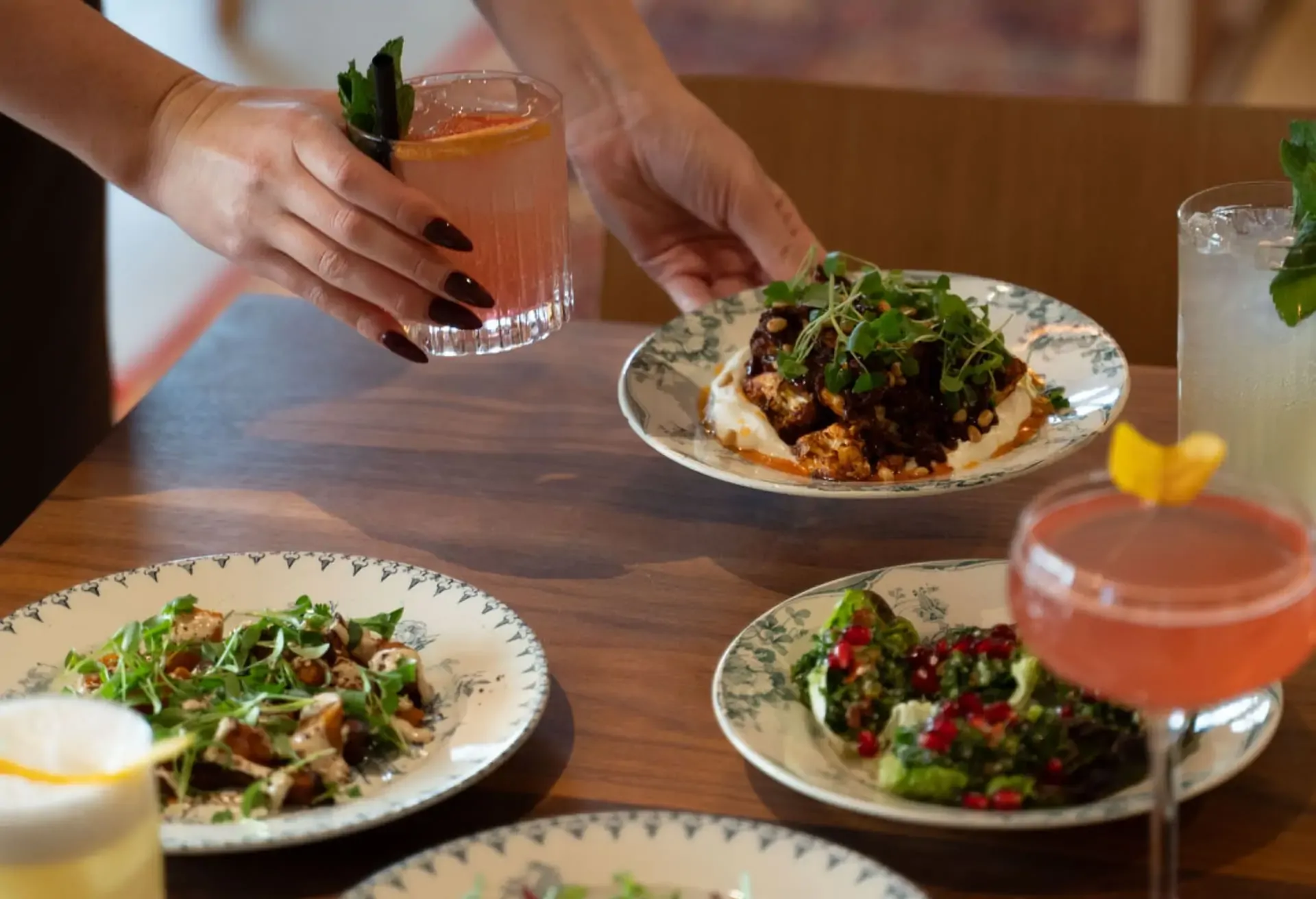 Hands serving cocktails and small gourmet plates at a restaurant.
