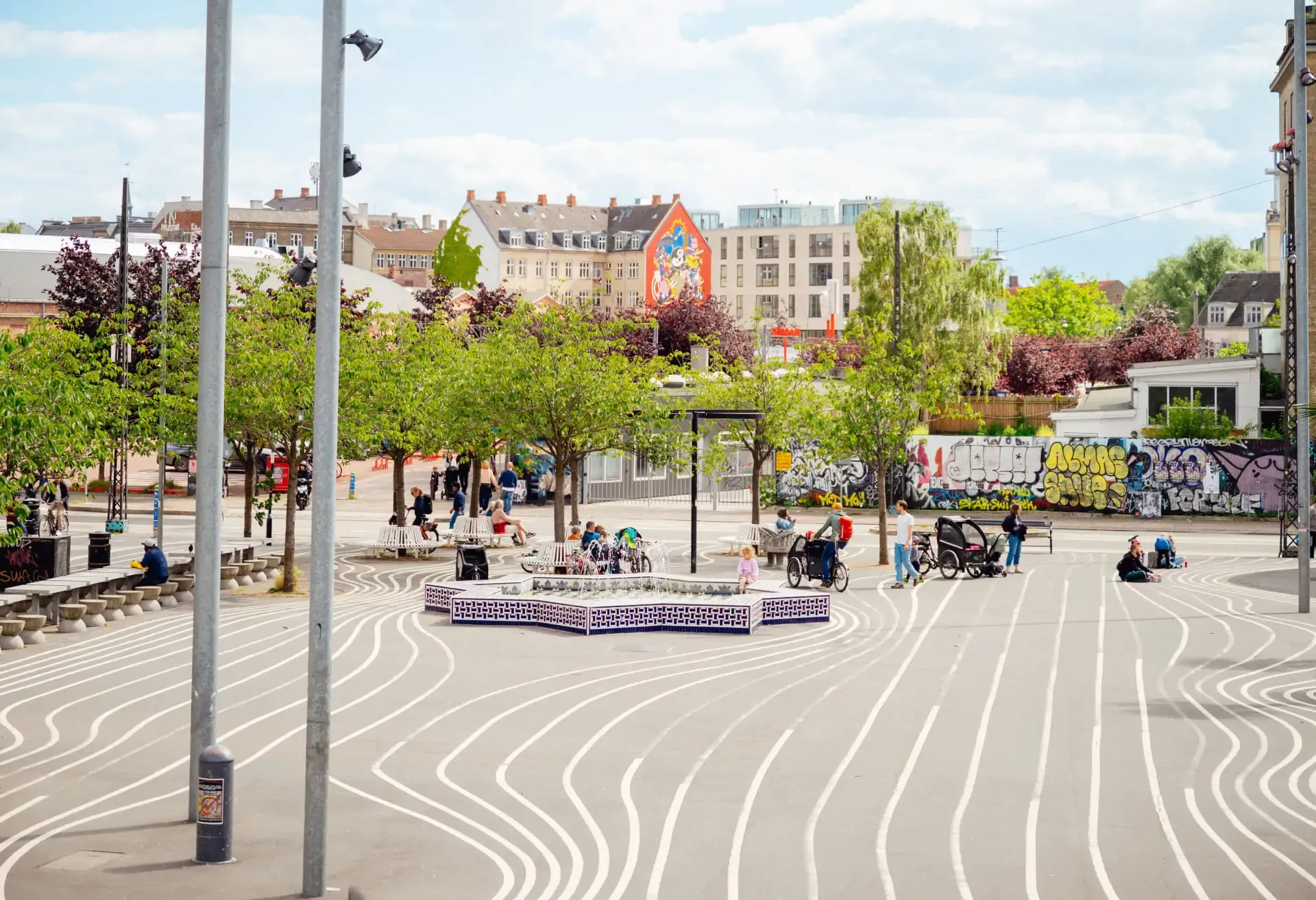 Public plaza with white wavy lines on the ground and lush green trees.