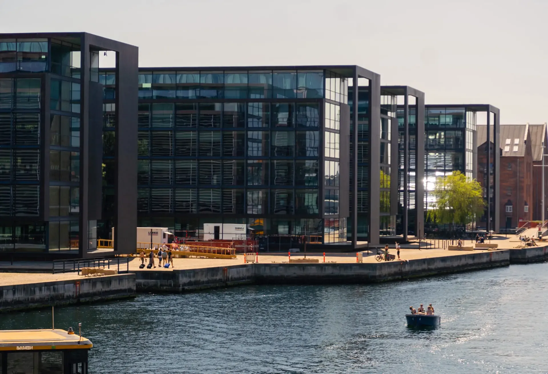Modern glass buildings on a waterfront with a small boat in the foreground.