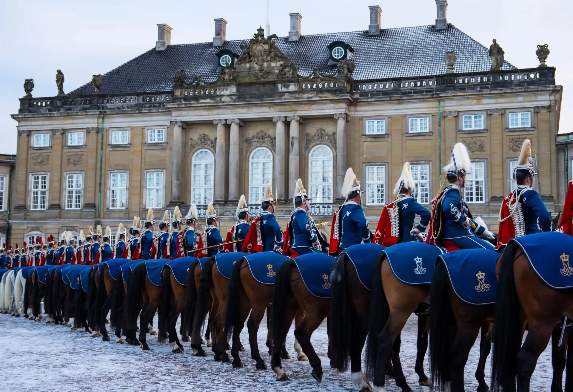 Royal guards on horseback parading in front of a grand, historic palace.
