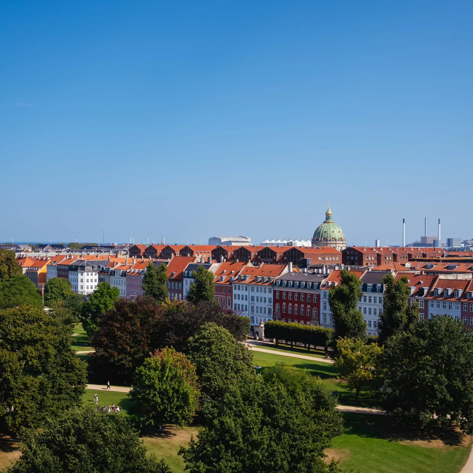 Panoramic view of a city with red roofs, a green dome, and a lush park.