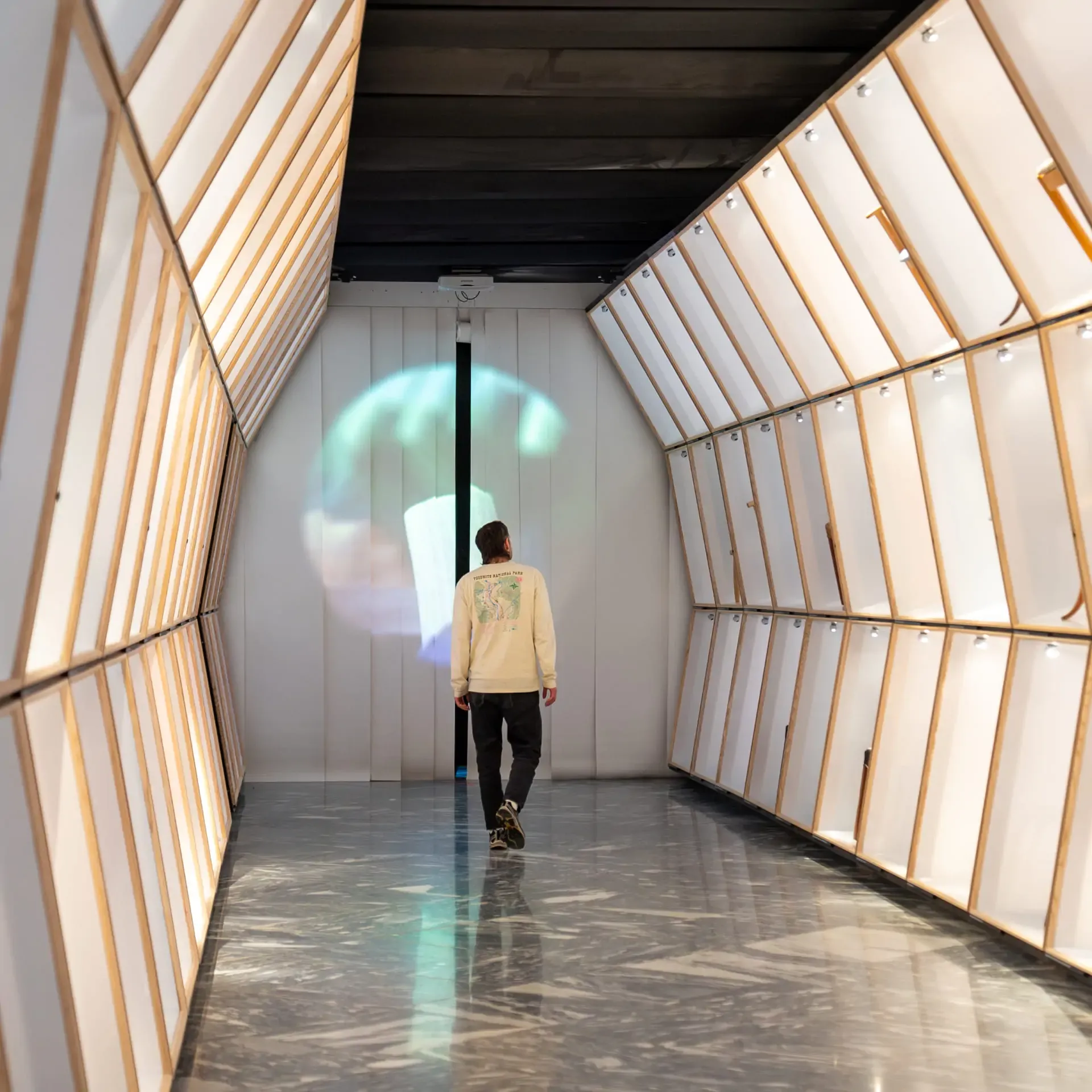 Man walking through a modern, backlit exhibition hall toward a circular projection.