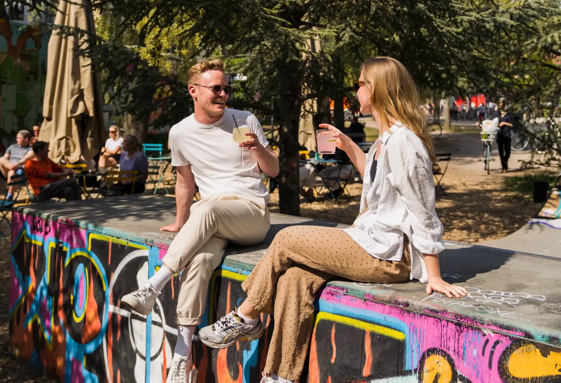 Man and woman laughing over drinks on a colorful graffiti ledge.