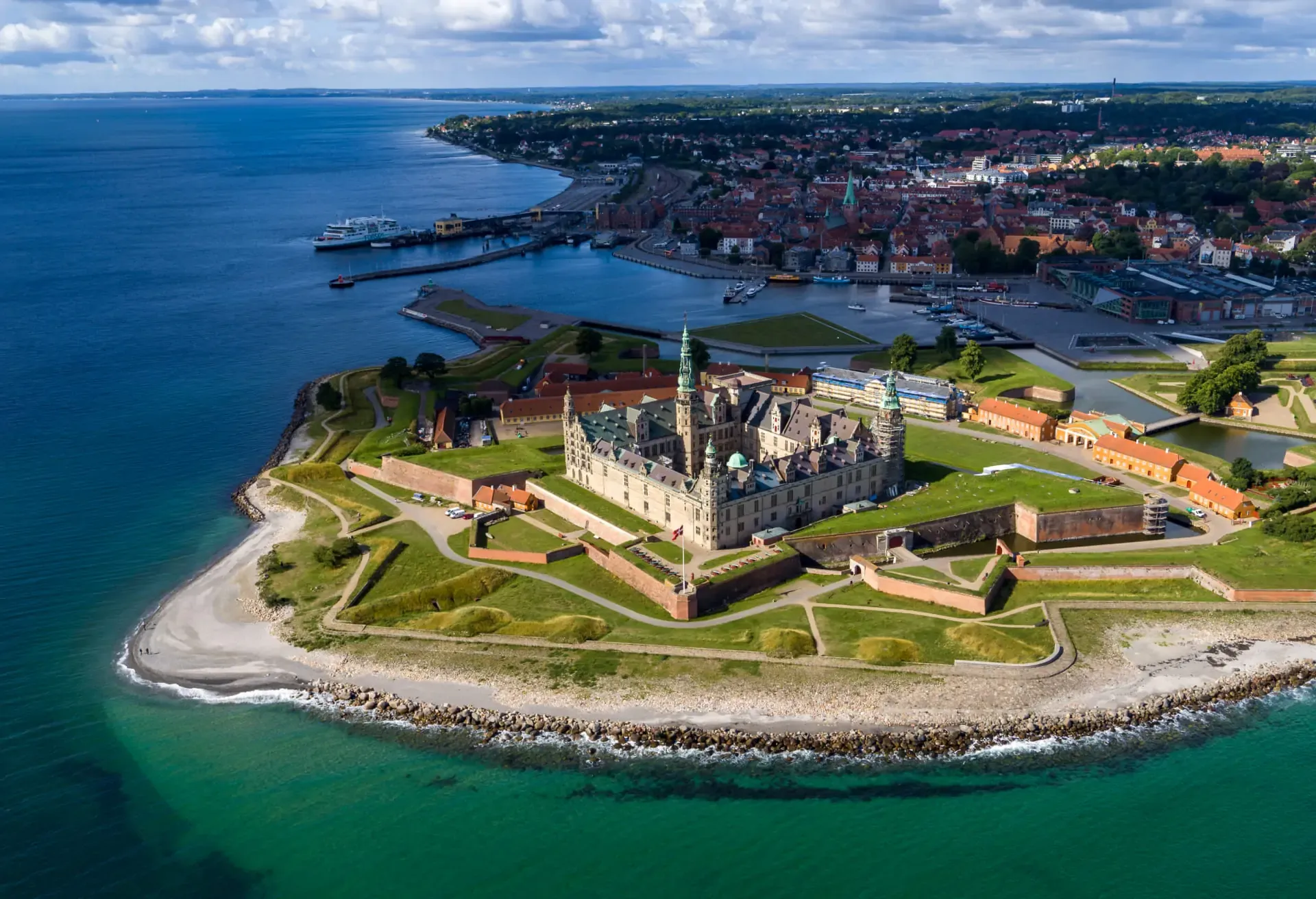 Aerial view of a historic castle on a coastal peninsula with turquoise water.