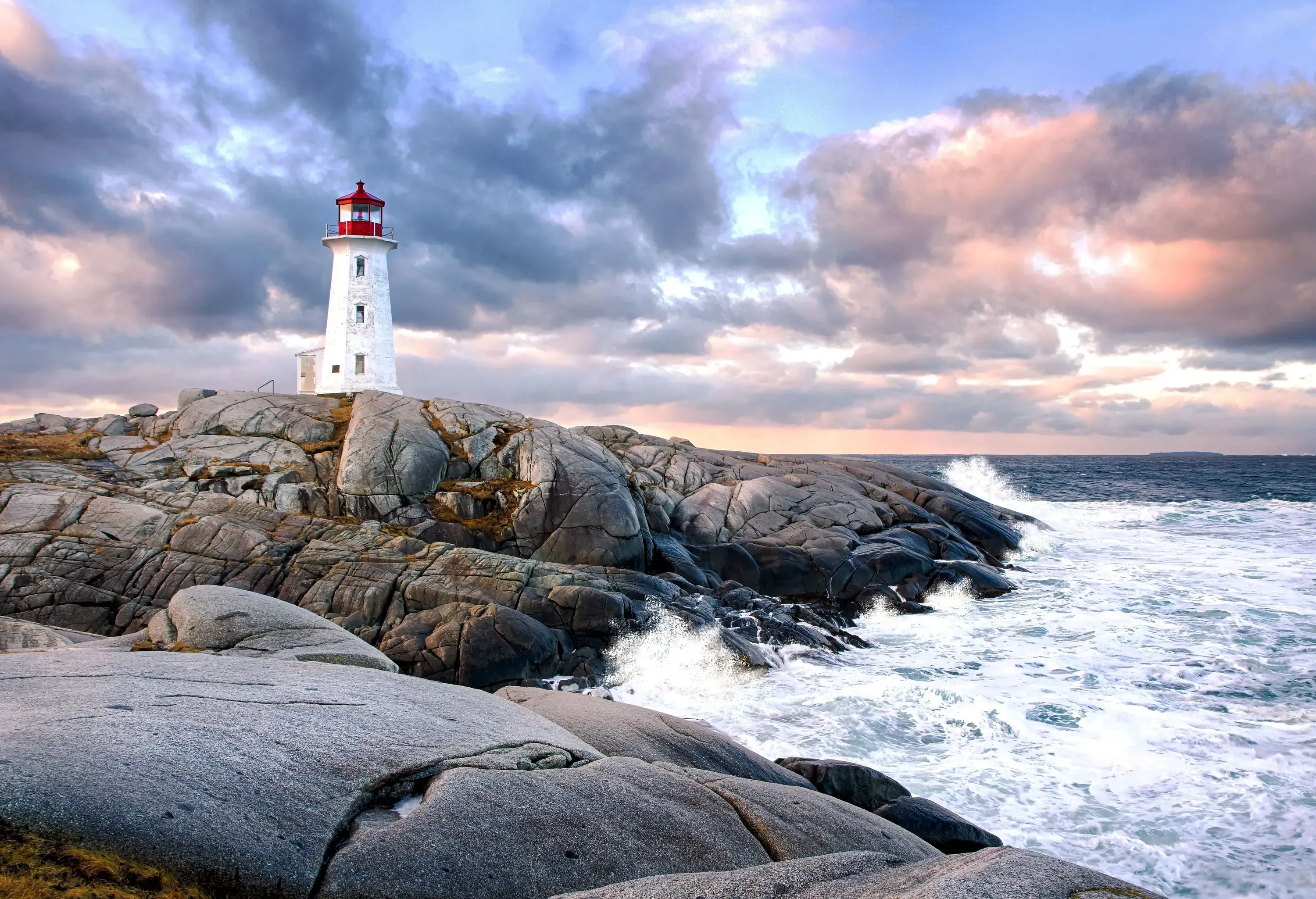 A white lighthouse at the edge of a rocky coastline with crashing ocean waves.